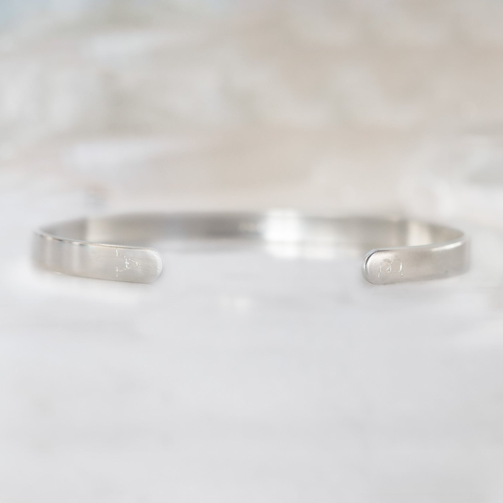 Custom Men's Cuff Bracelet | Sterling Silver. Displayed on marble surface with white blurred background.