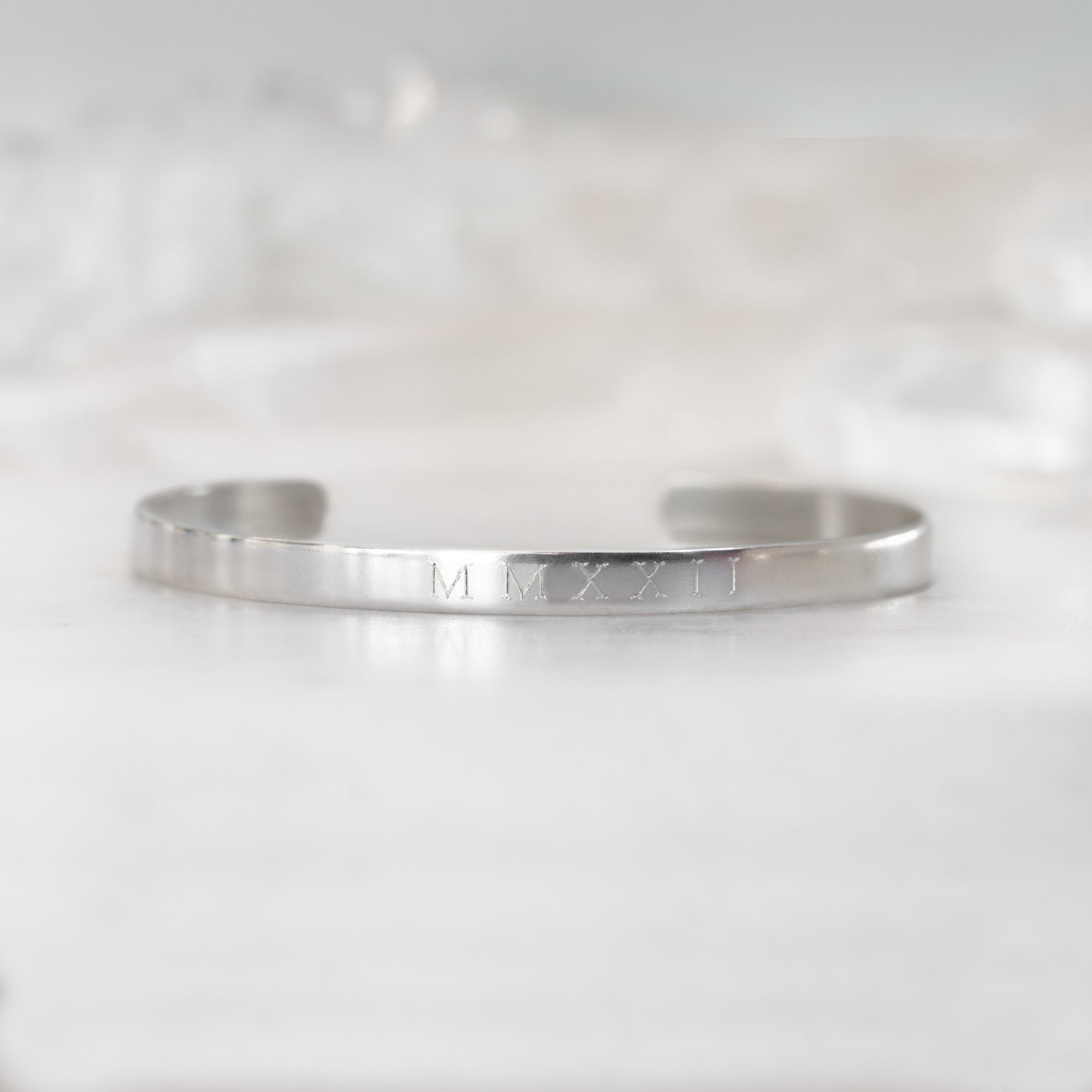 Custom Men's Cuff Bracelet | Sterling Silver. Displayed on marble surface with white blurred background.