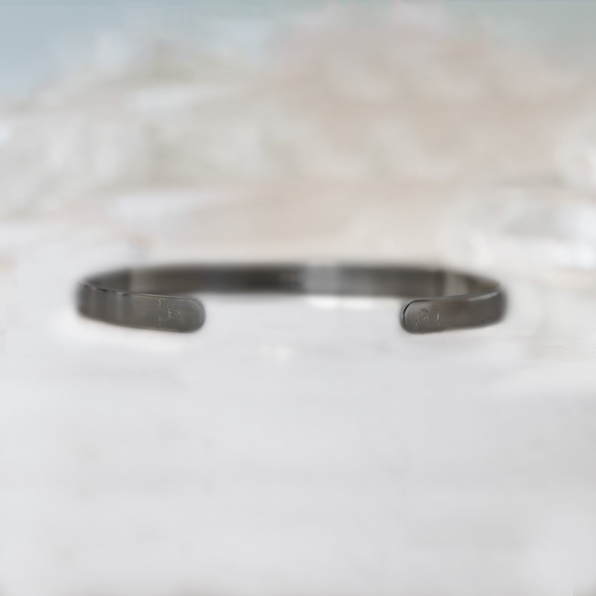 Custom Men's Cuff Bracelet | Oxidized Sterling Silver. Displayed on marble surface with white blurred background.