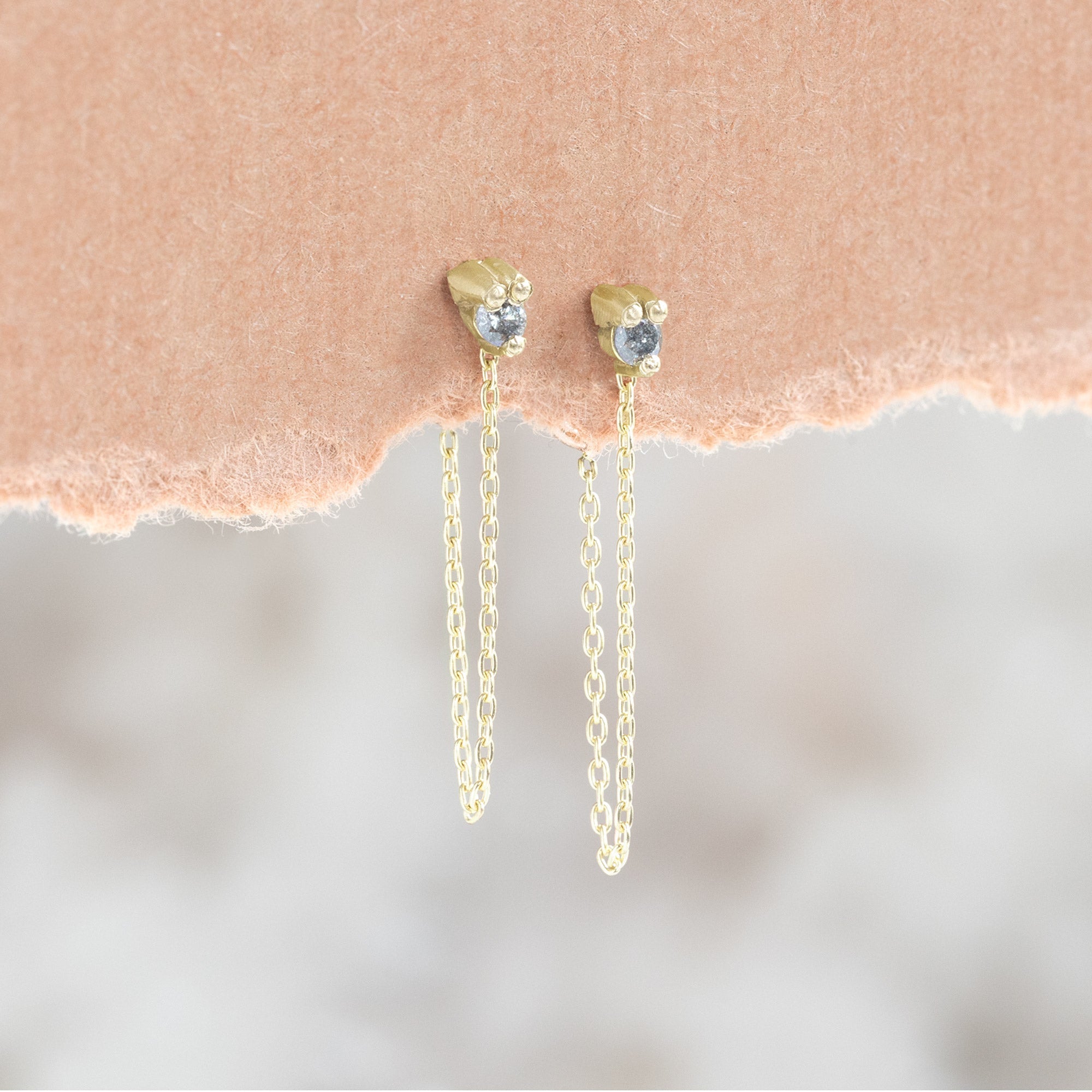 The Salt and Pepper Diamond Sunburst Chain Hoops in 10K Yellow Gold hanging on orange textured paper