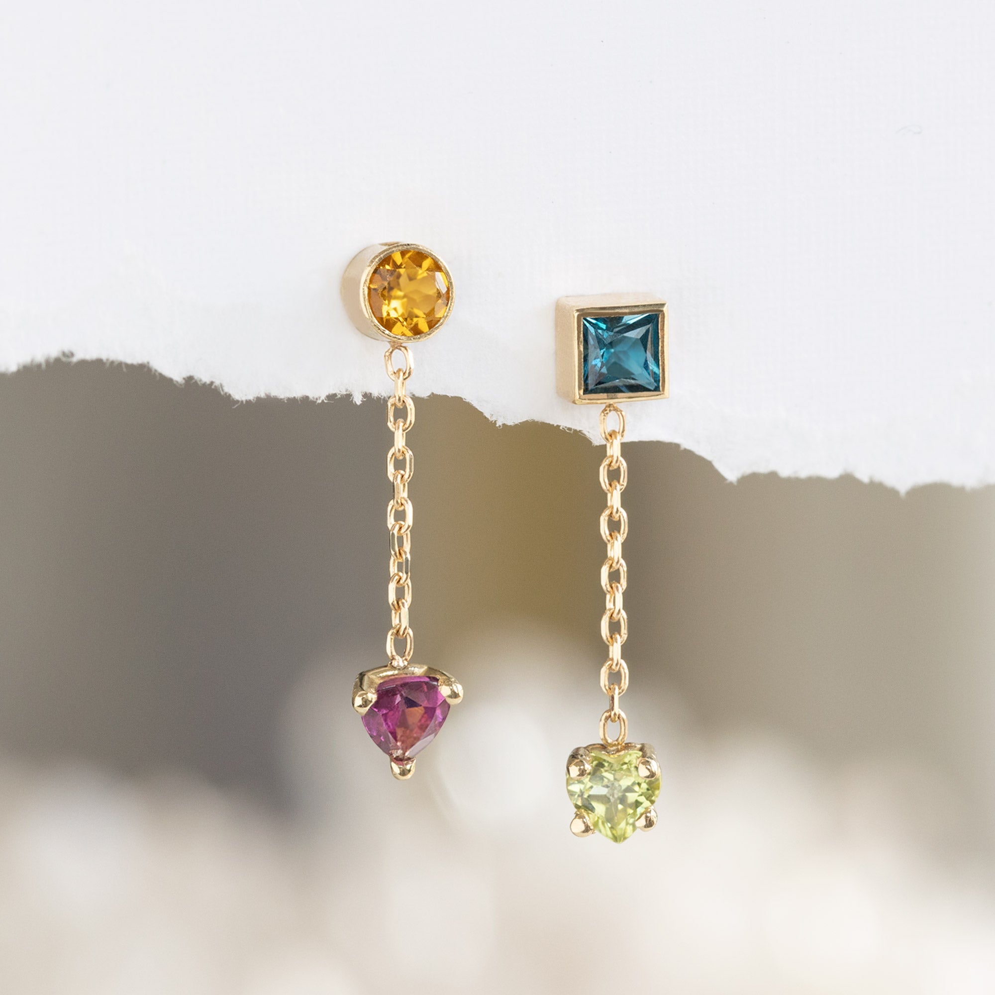 The Candy Gemstone Earrings in 10K Yellow Gold hanging on textured white paper