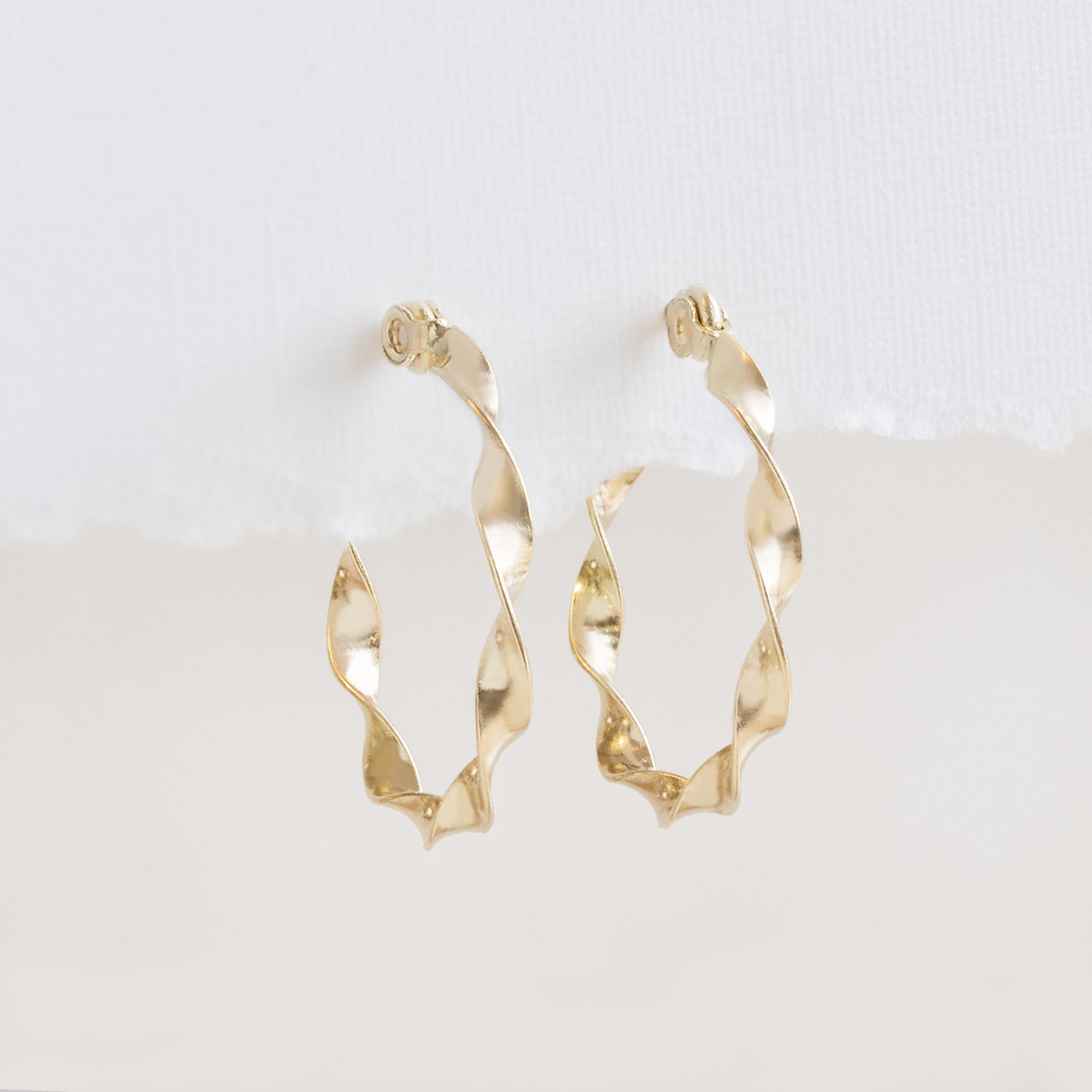 The Ribbon Hoops in 14K Yellow Gold hanging on textured white paper