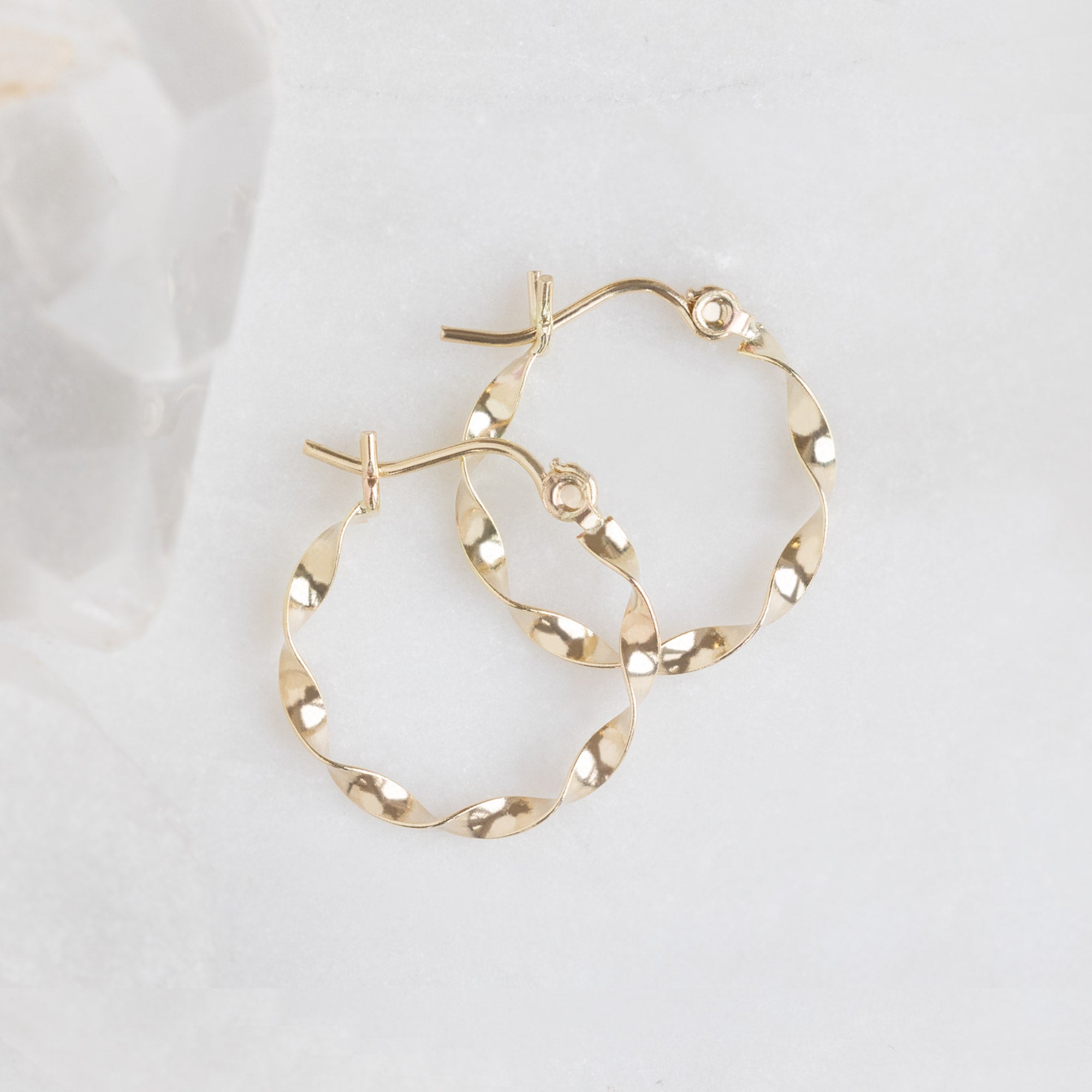 The Ribbon Hoops in 14K Yellow Gold laying on white marble
