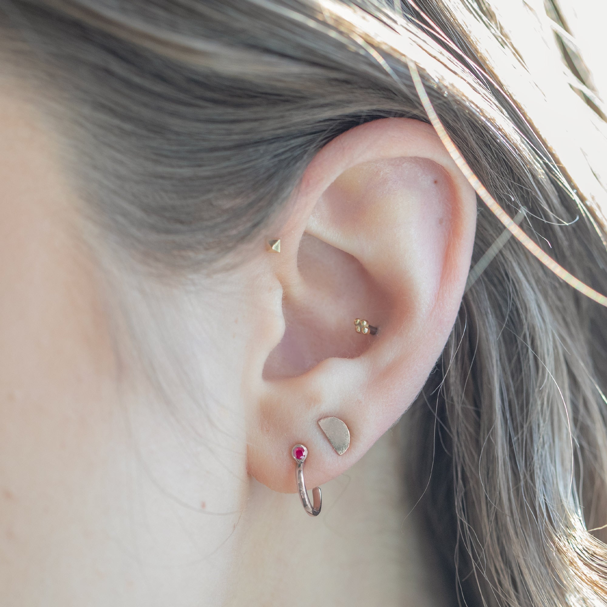 Displayed on holding bar with white blurred background. Displayed on model's ear with additional stud earrings.