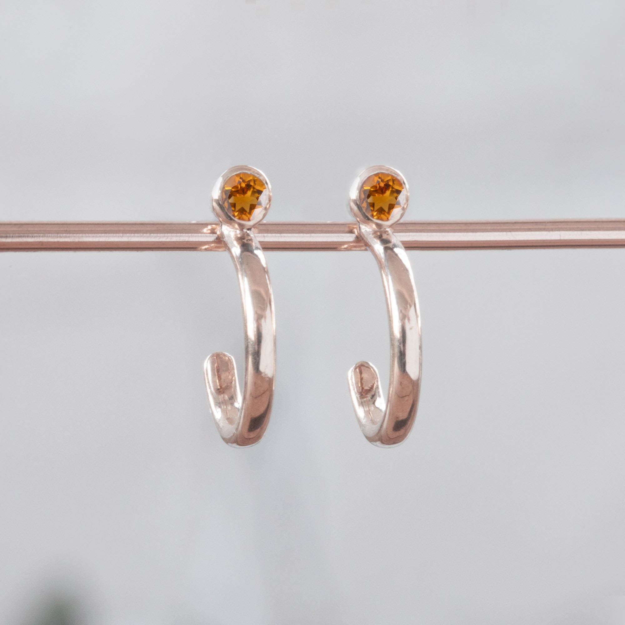 Custom Citrine Birthstone Hoop Earrings | 14K Rose Gold displayed on holding bar with white blurred background.