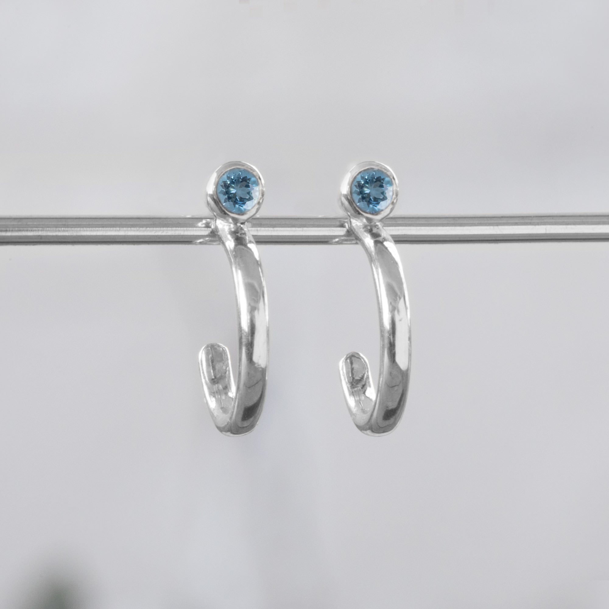 Custom Aquamarine Birthstone Hoop Earrings | 14K White Gold displayed on bar with white blurred background.