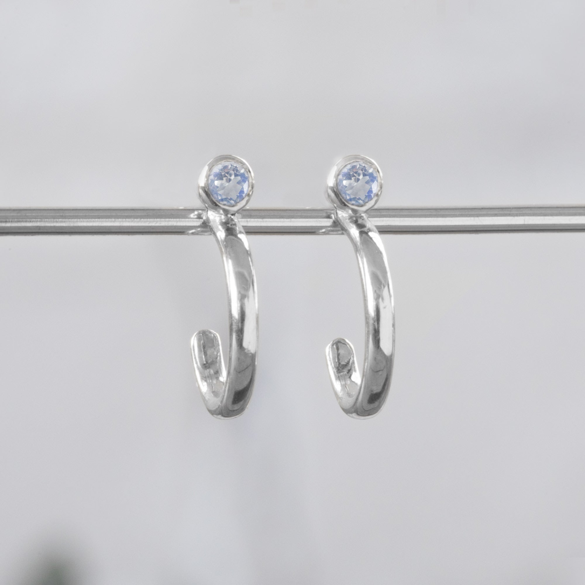 Custom Moonstone Birthstone Hoop Earrings | 14K White Gold. Displayed on holding bar with white blurred background.