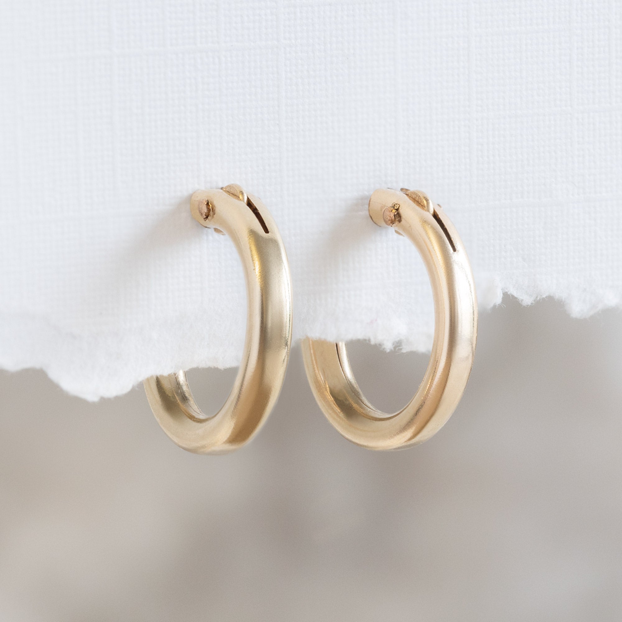 The Charm Hoop Earrings in Yellow Gold Filled hanging on torn white textured paper