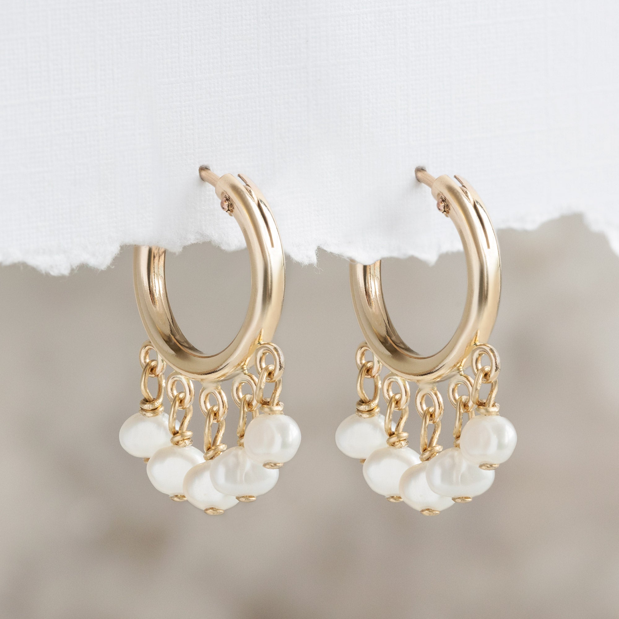 The Pearl Party Hoop Earrings in Yellow Gold Filled hanging on textured white paper