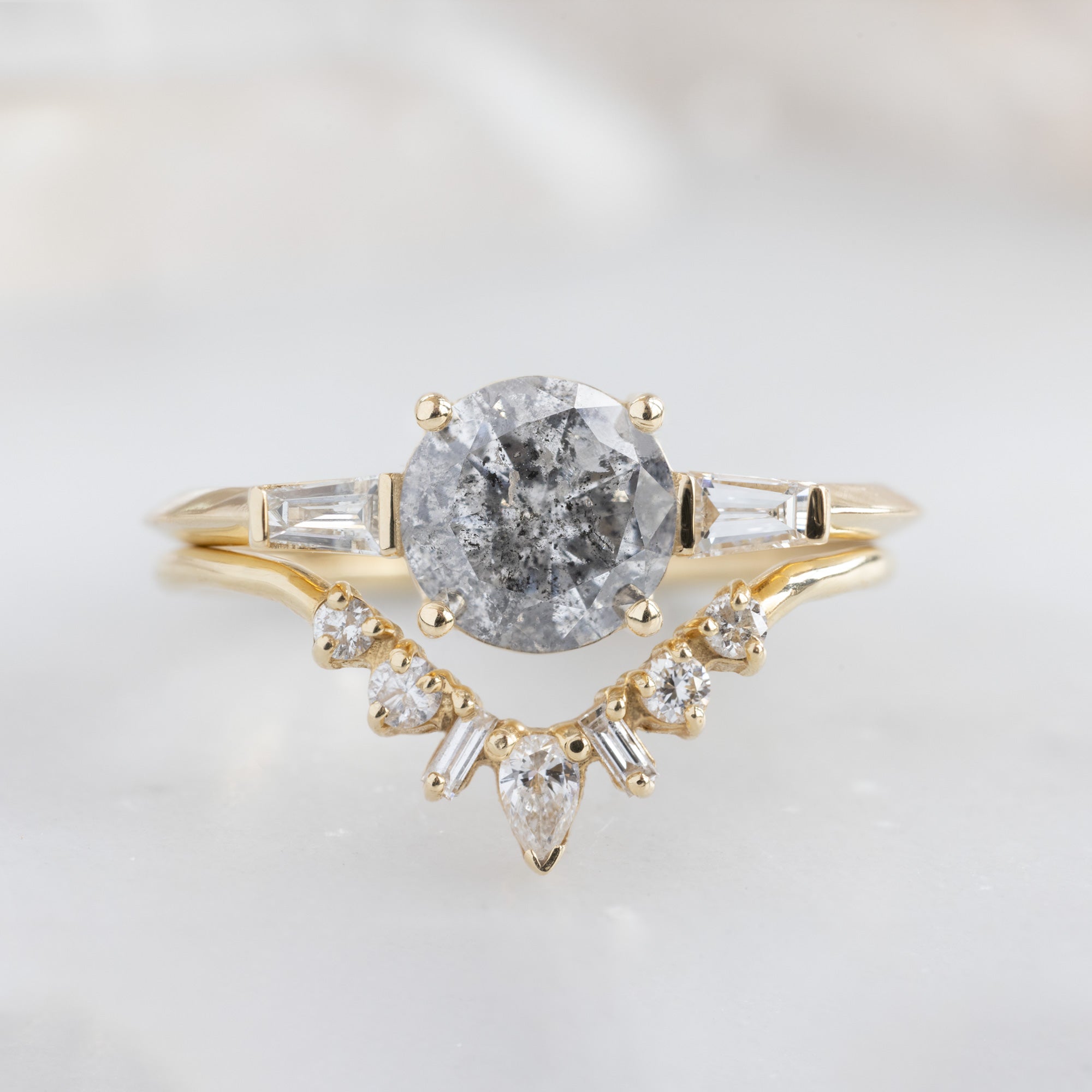 The Ash Ring | 1.22 carat Round Salt and Pepper Diamond in 14K Yellow Gold with white blurred background. Displayed upon the geometric white diamond sunburst stacking ring.