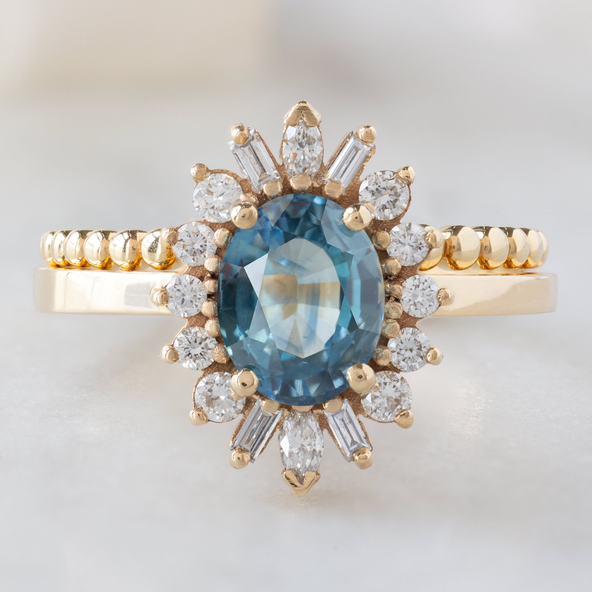 The Camellia Ring with a 1.32ct Oval Blue Montana Sapphire in 14K Yellow Gold Stacked with the Beaded Stacking Band