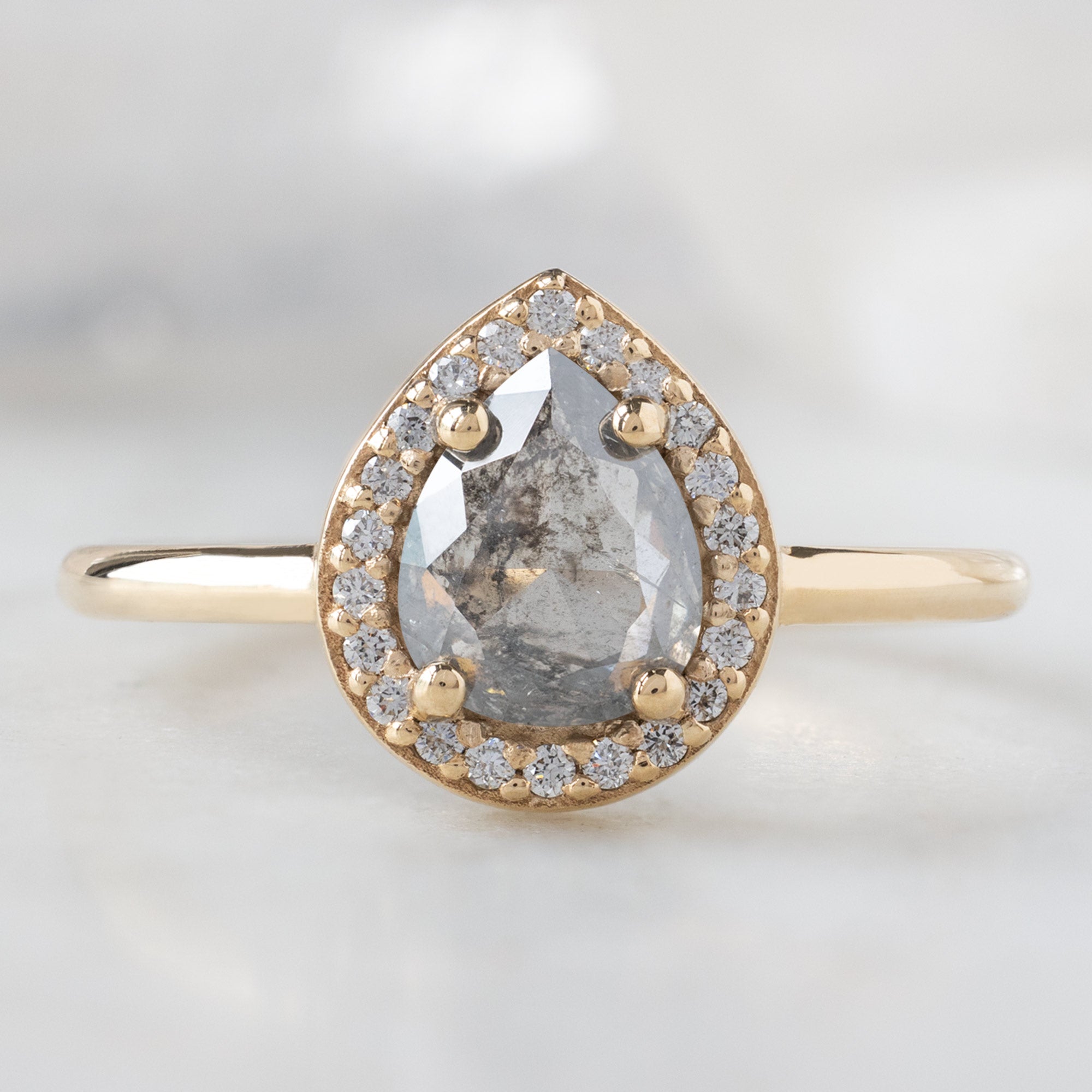 The Dahlia Ring with a 0.90ct Pear Grey Diamond in 14K Yellow Gold on White Marble