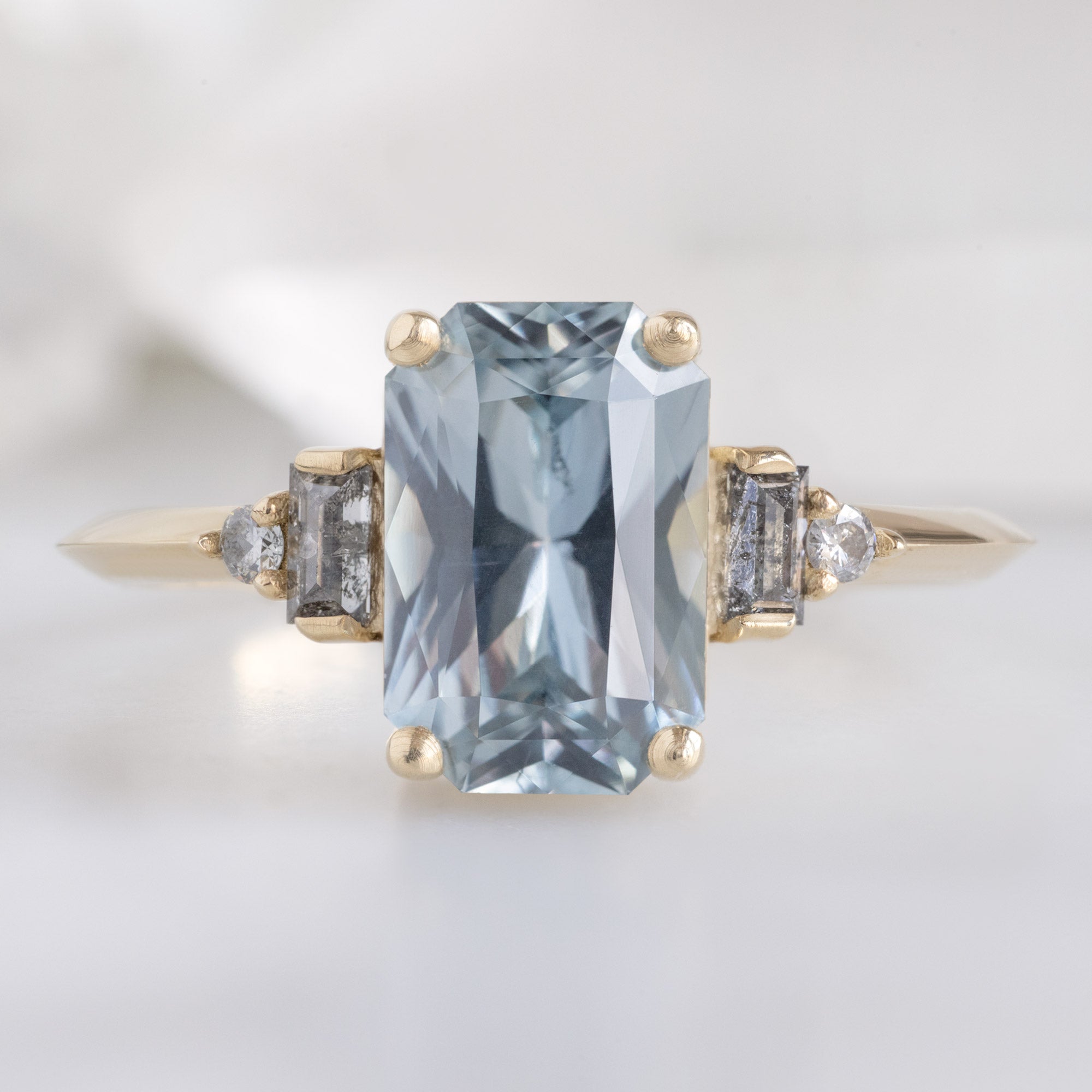 The Primrose Ring with a 2.00ct Emerald-Cut Blue Sapphire in 14K Yellow Gold on White Marble