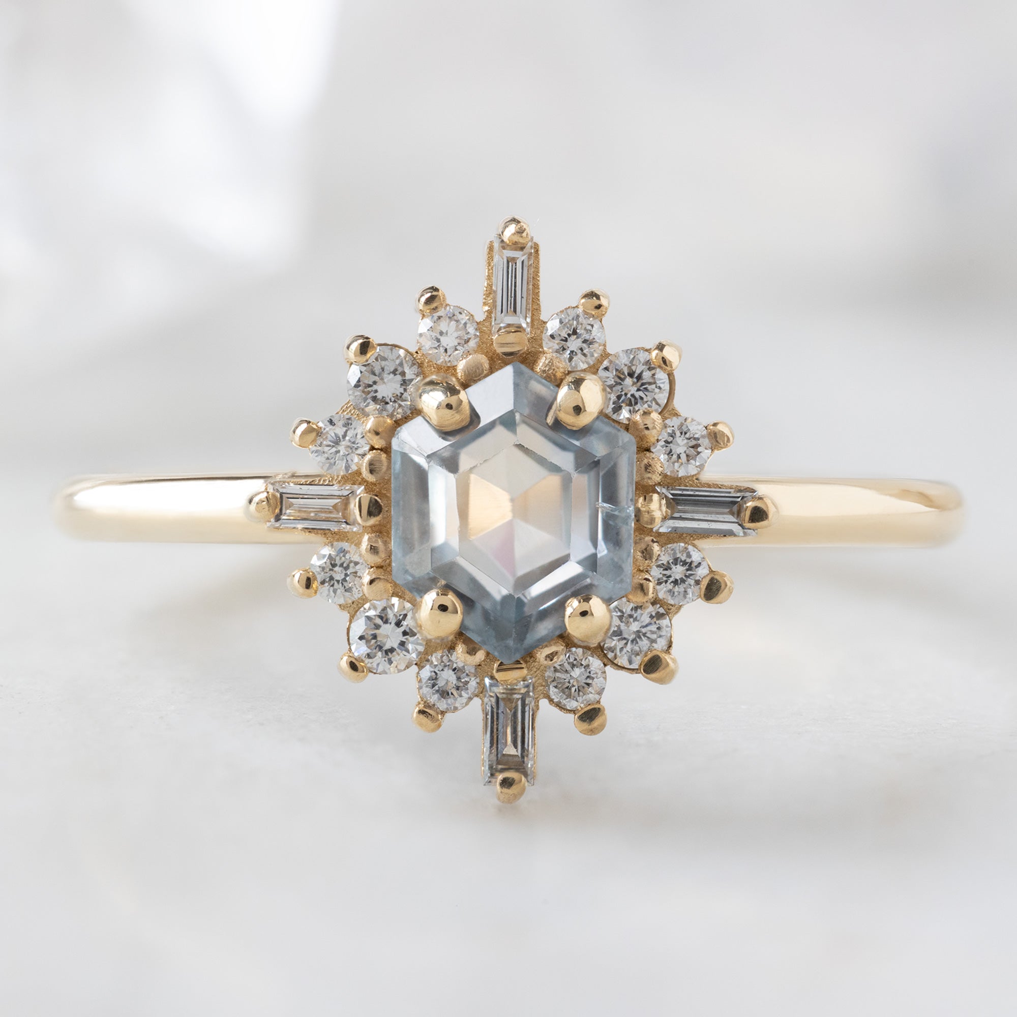 The Compass Ring with a 0.75ct Hexagon Grey Sapphire in 14K Yellow Gold on White Marble