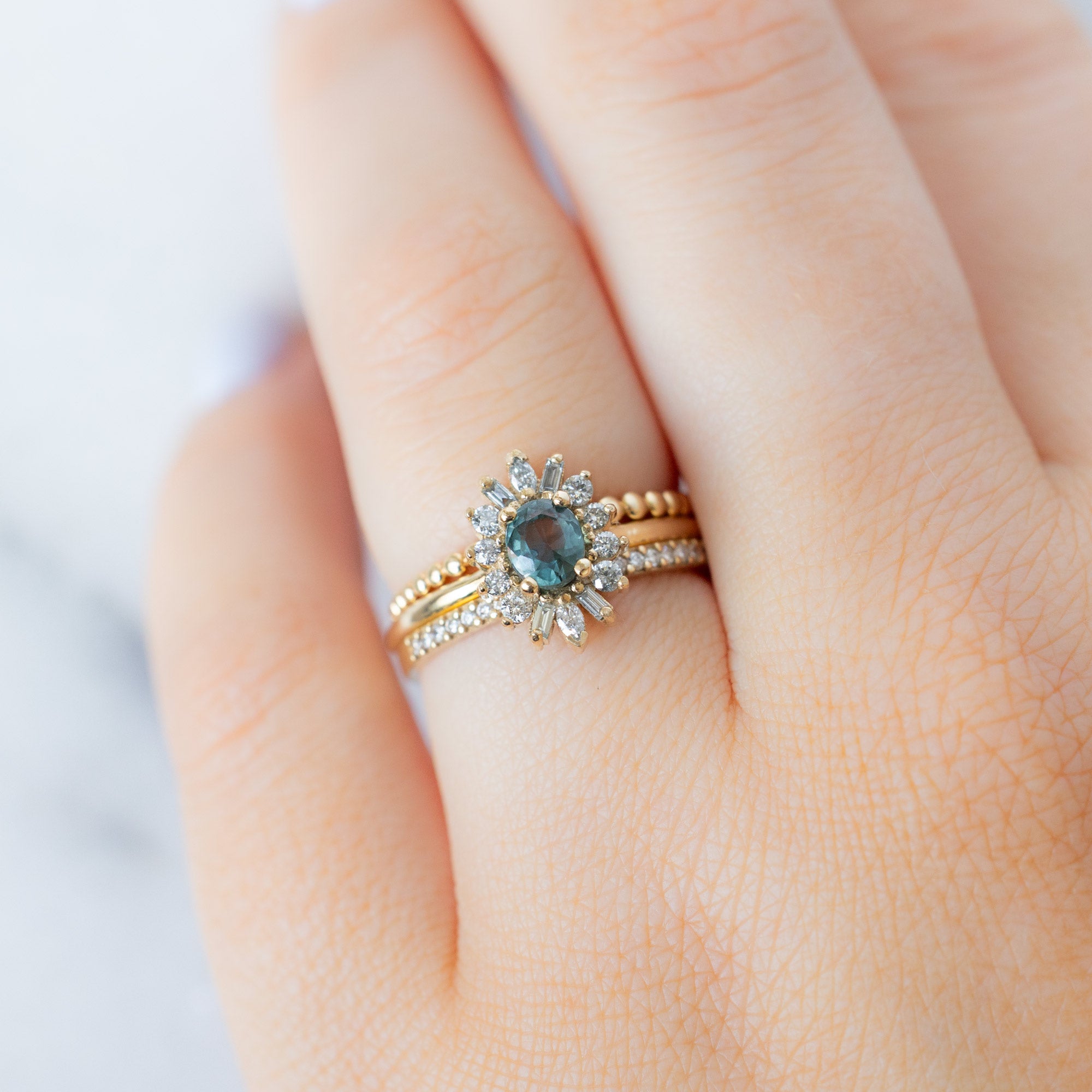 The Camellia Ring with an Oval Cut Blue Sapphire in 14K Yellow Gold Stacked with Wedding Bands on Model