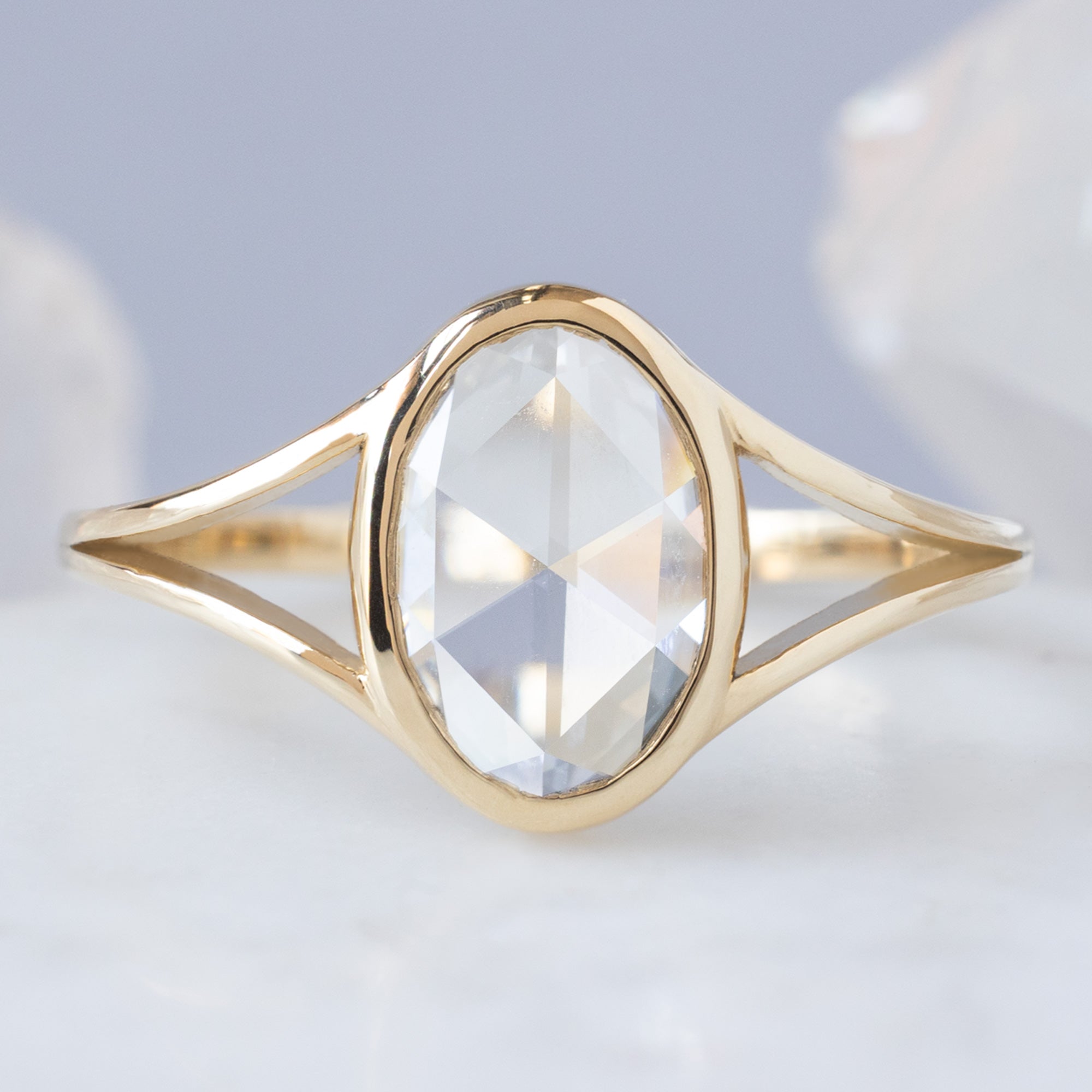 The Magnolia Ring with a 1.26ct Oval Lab Grown White Diamond in 14K Yellow Gold on Pale Blue Bbackground
