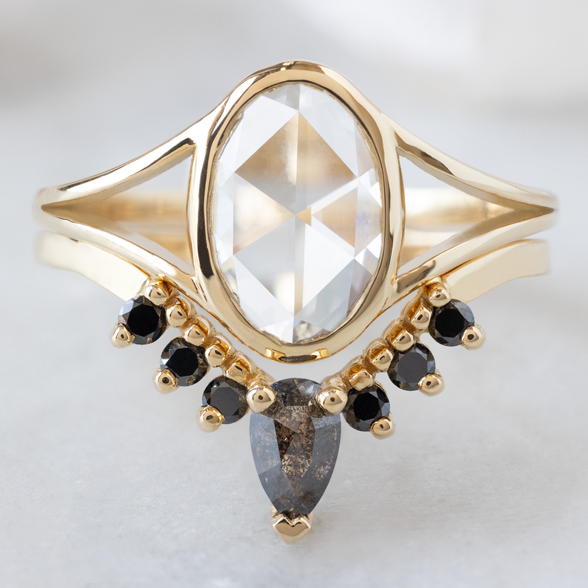 The Magnolia Ring with a 1.26ct Oval Lab Grown White Diamond in 14K Yellow Gold Stacked with the Black Diamond Sunburst Wedding Band on White Background