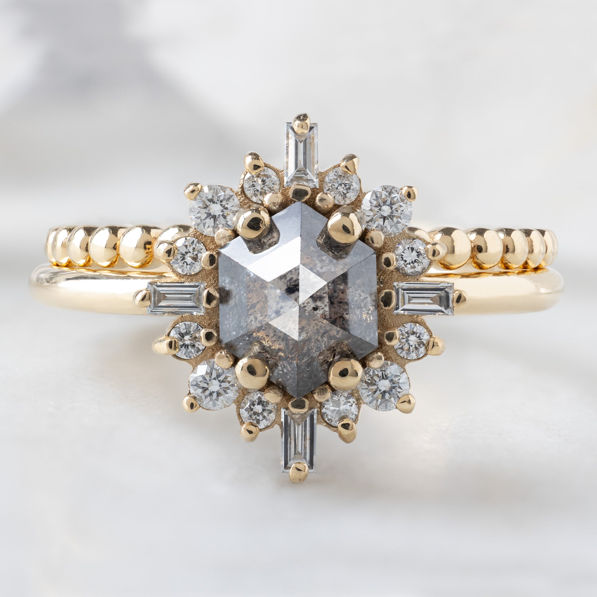 The Compass Ring with a 0.86ct Hexagon Salt and Pepper Diamond in 14K Yellow Gold Stacked with the Beaded Stacking Band on White Marble