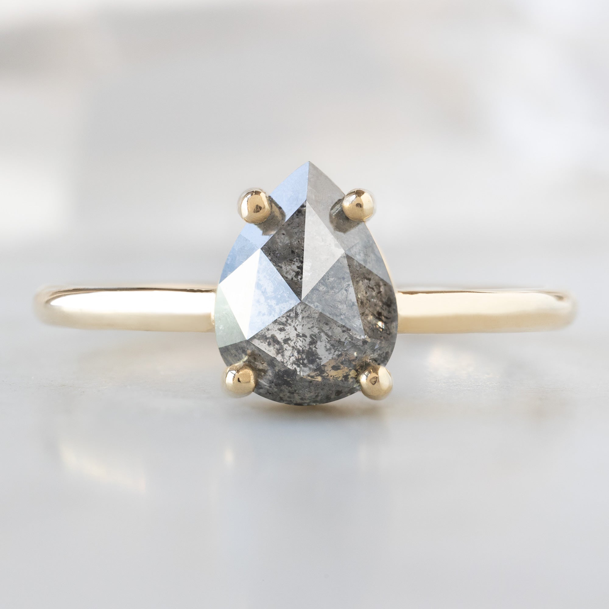The Bryn Ring with a 1.25ct Pear Salt and Pepper Diamond in 14K Yellow Gold on White Marble