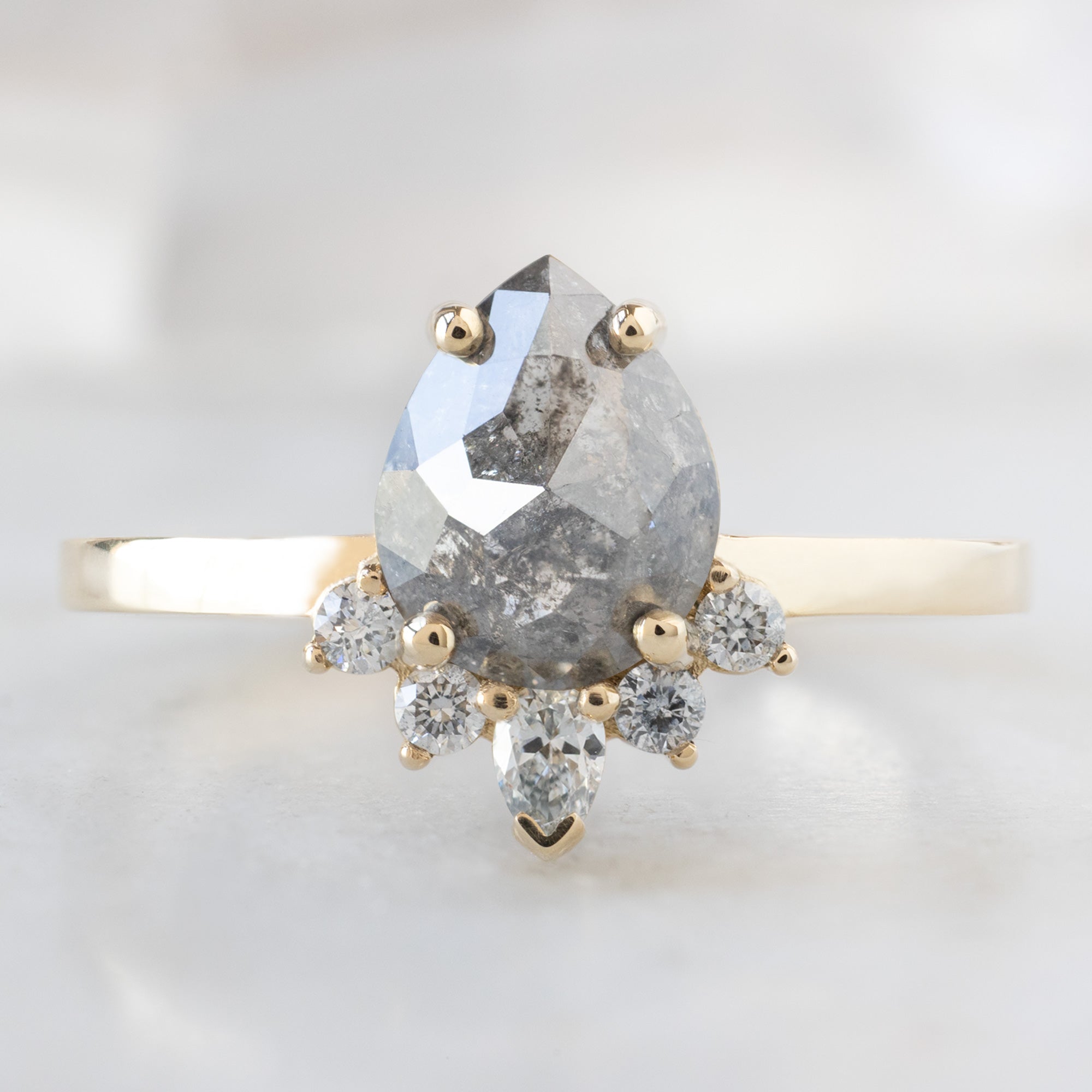 The Aster Ring with a 1.31ct Pear Salt and Pepper Diamond in 14K Yellow Gold on White Marble