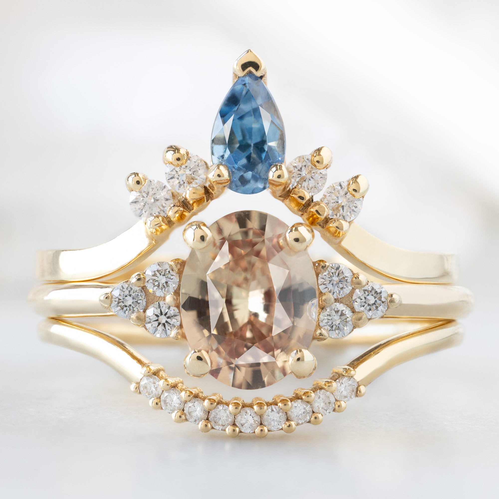 The Ivy Ring with a 1.13ct Oval Peach Sapphire in 14K Yellow Gold Stacked with Blue Sapphire and White Diamond Sunburst Stacking Band and White Diamond PAvé Arc Stacking Band