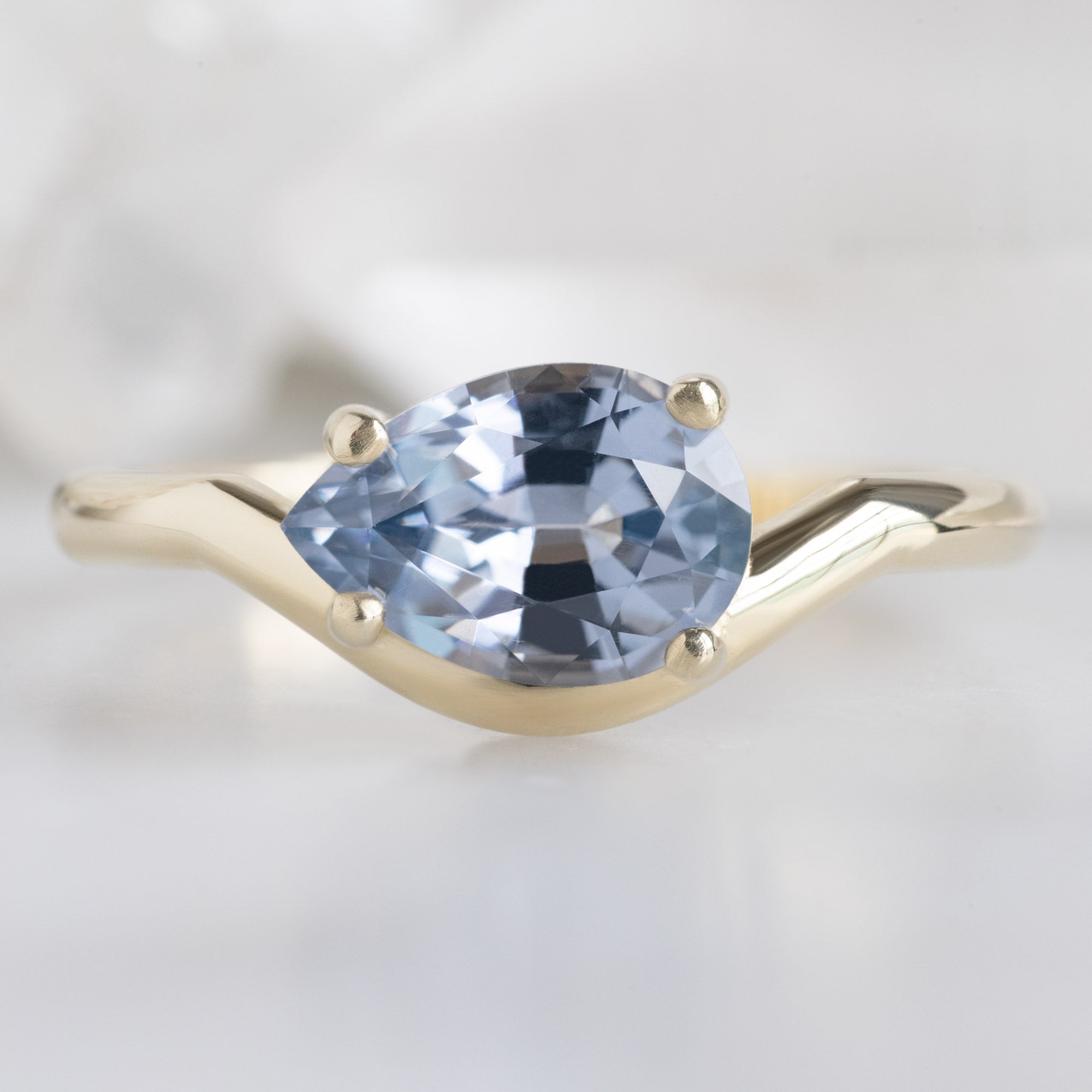 The Wave Ring with a 1.29ct Pear Lavender Spinel in 14k Yellow Gold on White Marble Surface
