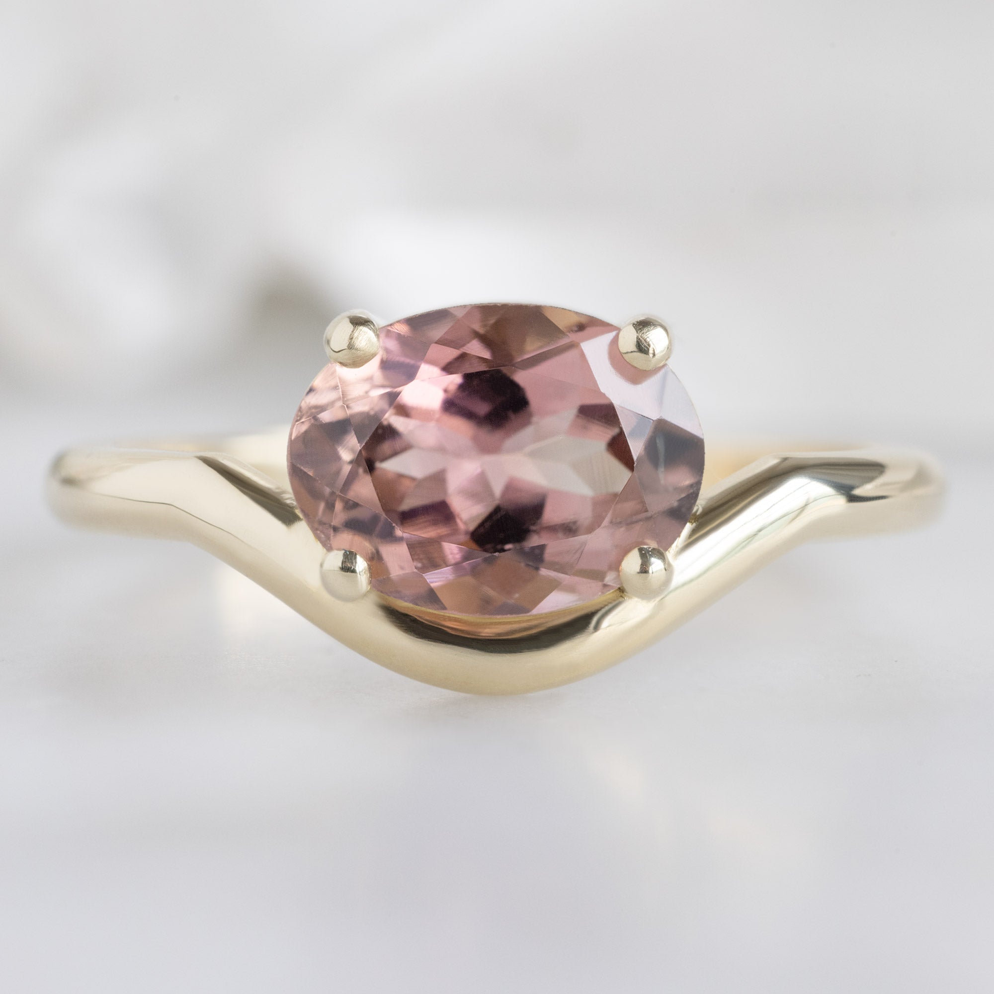 The Wave Ring with a 1.35ct Oval Pink Tourmaline in 14k Yellow Gold on White Marble Surface