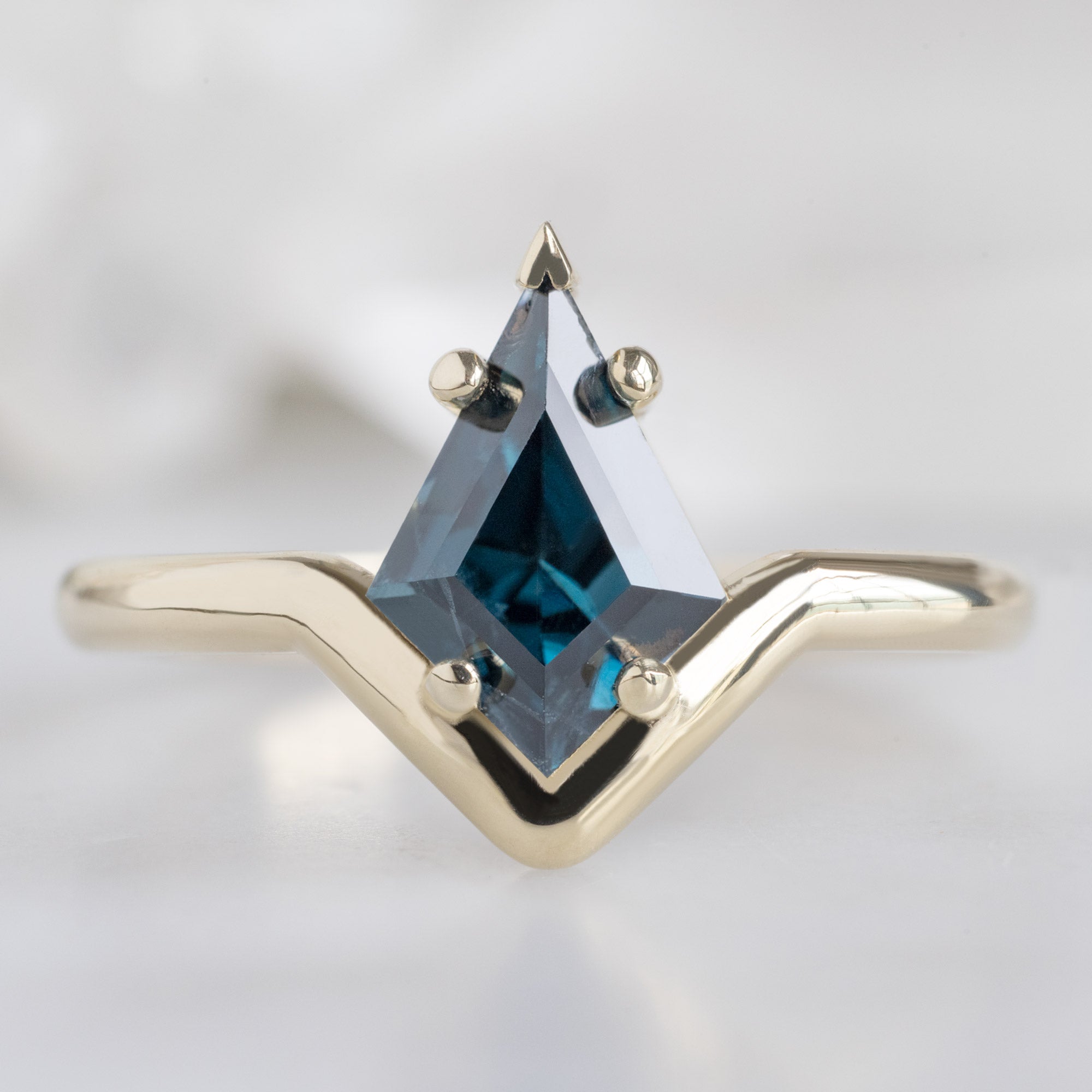 The Wave Ring with a 1.08ct Kite Blue Spinel in 14k Yellow Gold on White Marble Surface