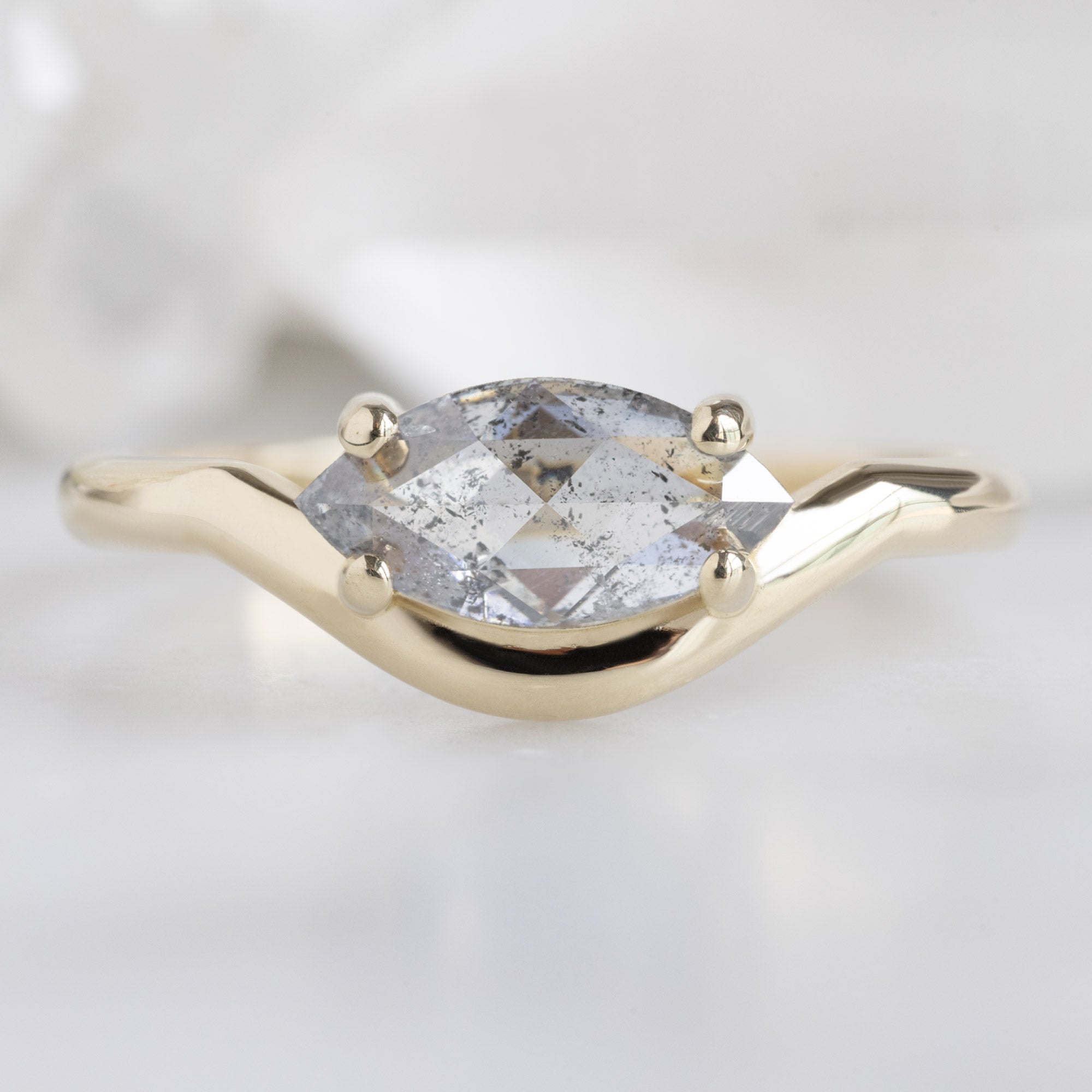The Wave Ring with a 0.72ct Marquise Salt and Pepper Diamond in 14K Yellow Gold on White Marble Surface