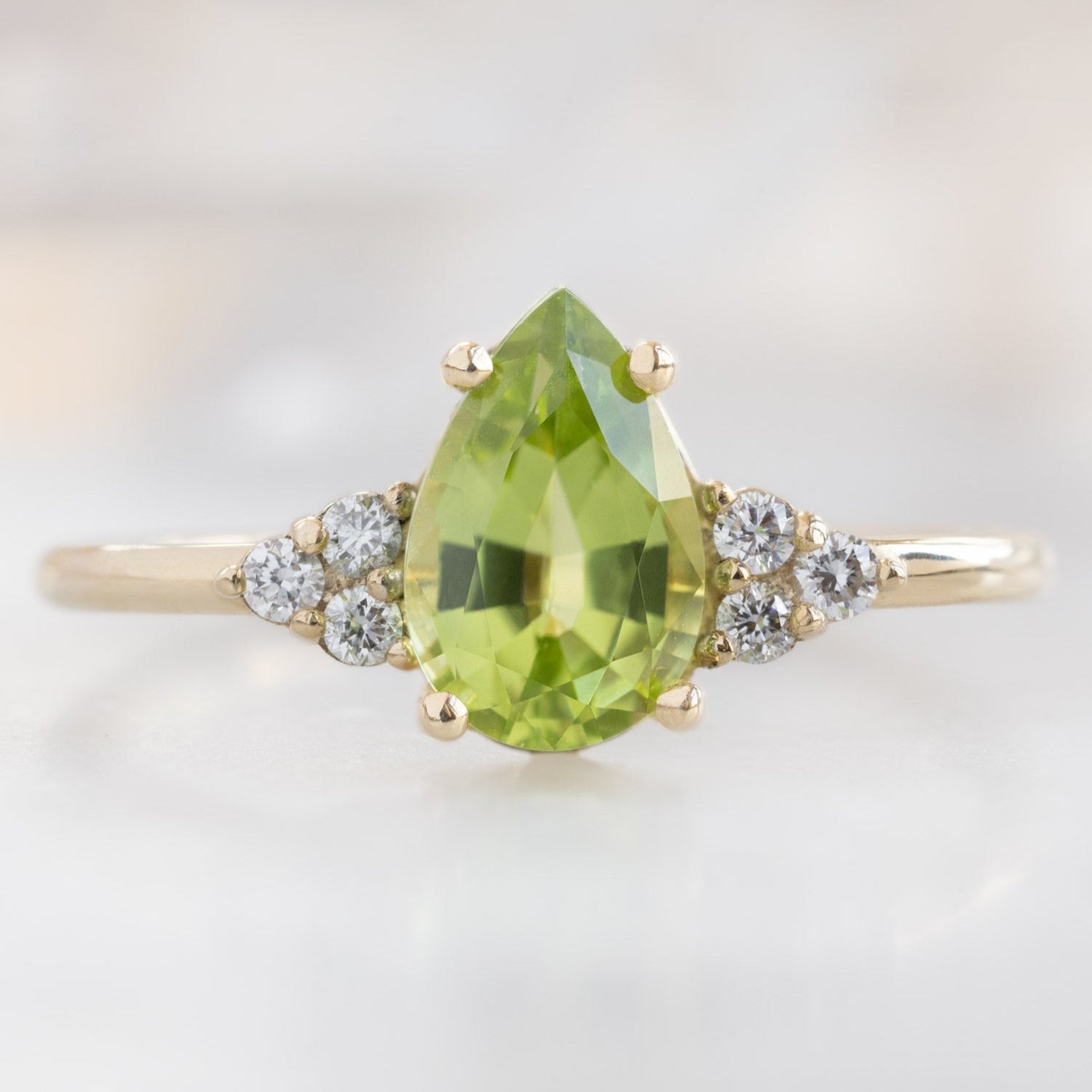 The Ivy Ring with a .89ct Pear Peridot in 14K Yellow Gold on White Marble Surface