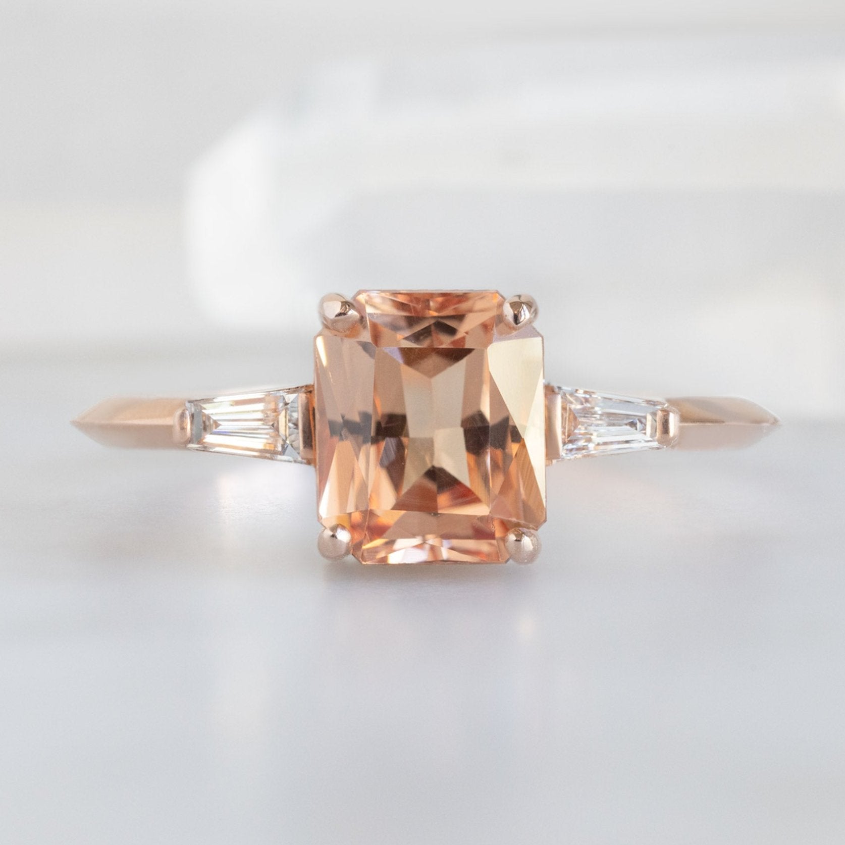 The Ash Ring with a 1.43ct Emerald Cut Garnet in 14K Rose Gold displayed on marble surface.