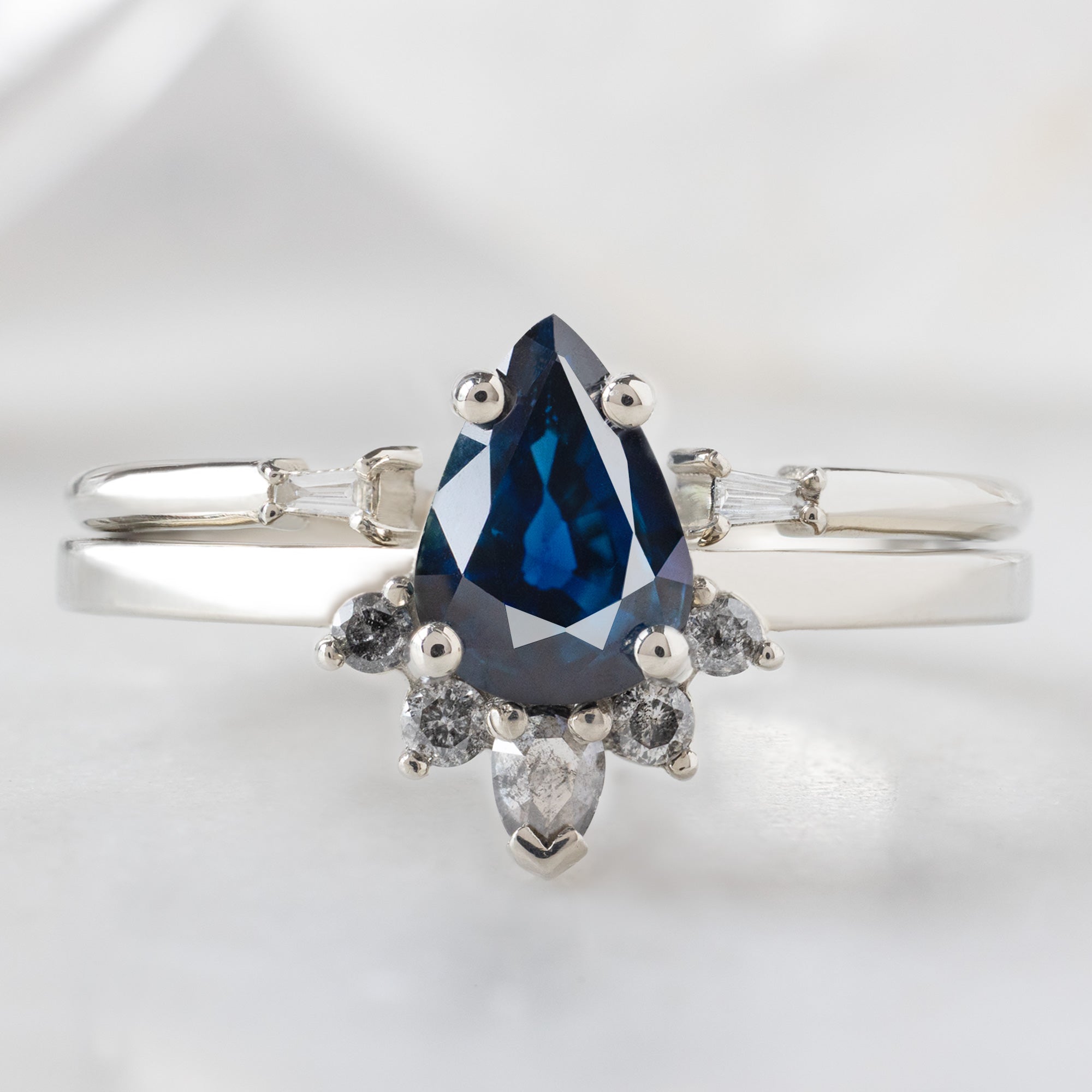 The Aster Ring with a 0.90ct Pear Blue Sapphire in 14K White Gold Stacked with the Open Cuff White Diamond Baguette Stacking Band on White Background