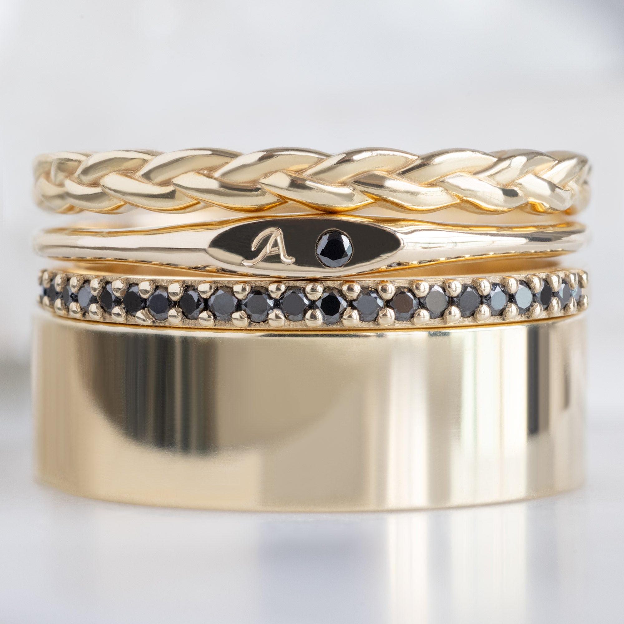 The Teensy Black Diamond Signet Ring in 10K Yellow Gold Stacked with Wedding Bands on White Marble