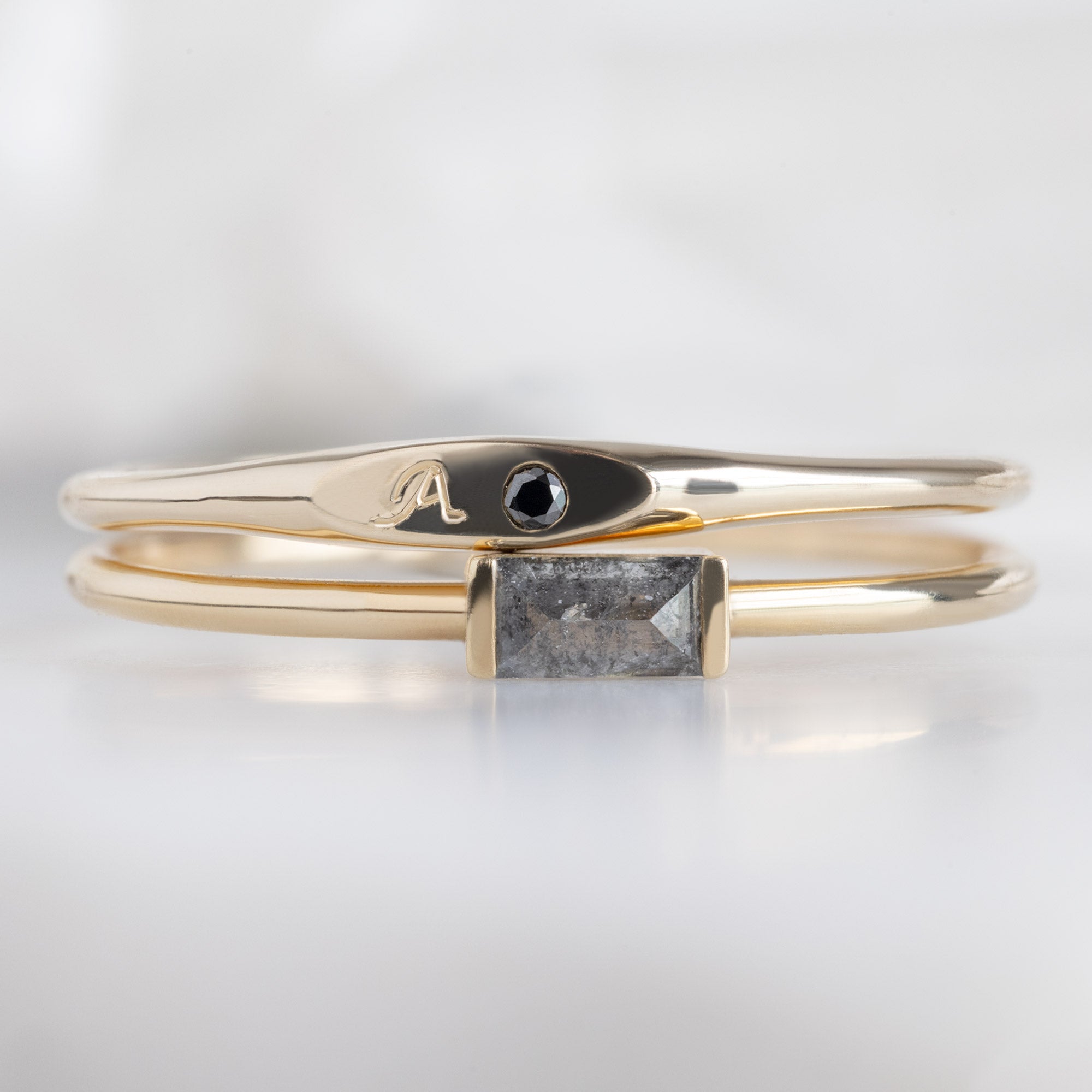 The Teensy Black Diamond Signet Ring in 10K Yellow Gold Stacked on top of the Salt and Pepper Diamond Line Ring on White Marble