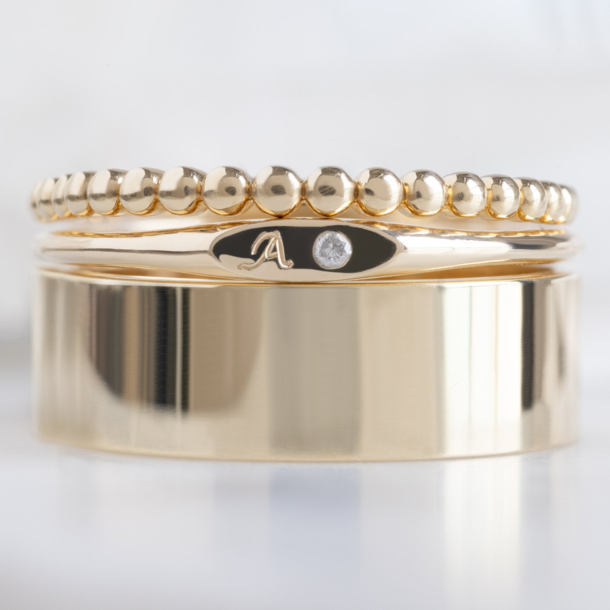 The Teensy White Diamond Signet Ring in 10K Yellow Gold Stacked with Classic Gold Bands on White Marble