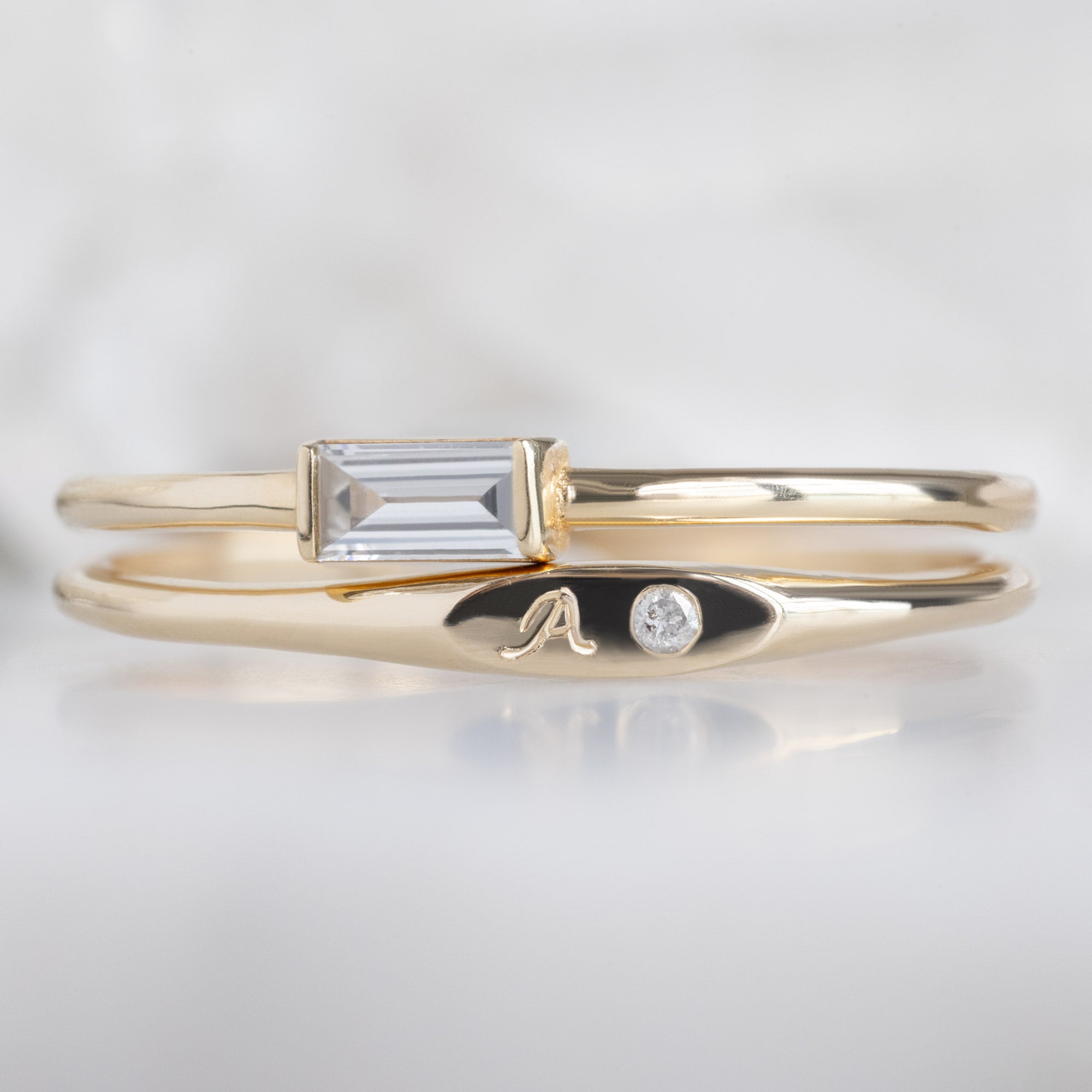 The Teensy White Diamond Signet Ring in 10K Yellow Gold Stacked with the White Diamond Baguette Line Ring on White Marble