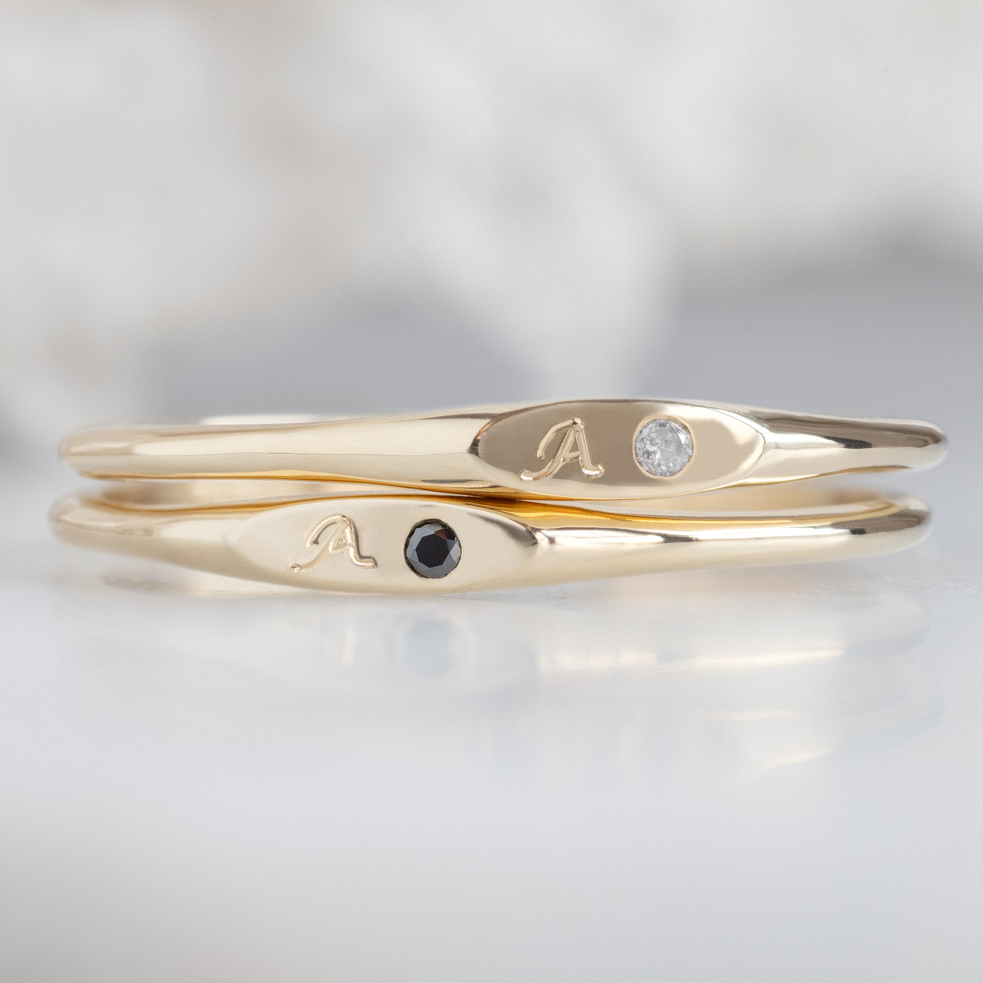 The Teensy White and Black Diamond Signet Rings in 10K Yellow Gold Stacked on Top of Each Other on White Marble