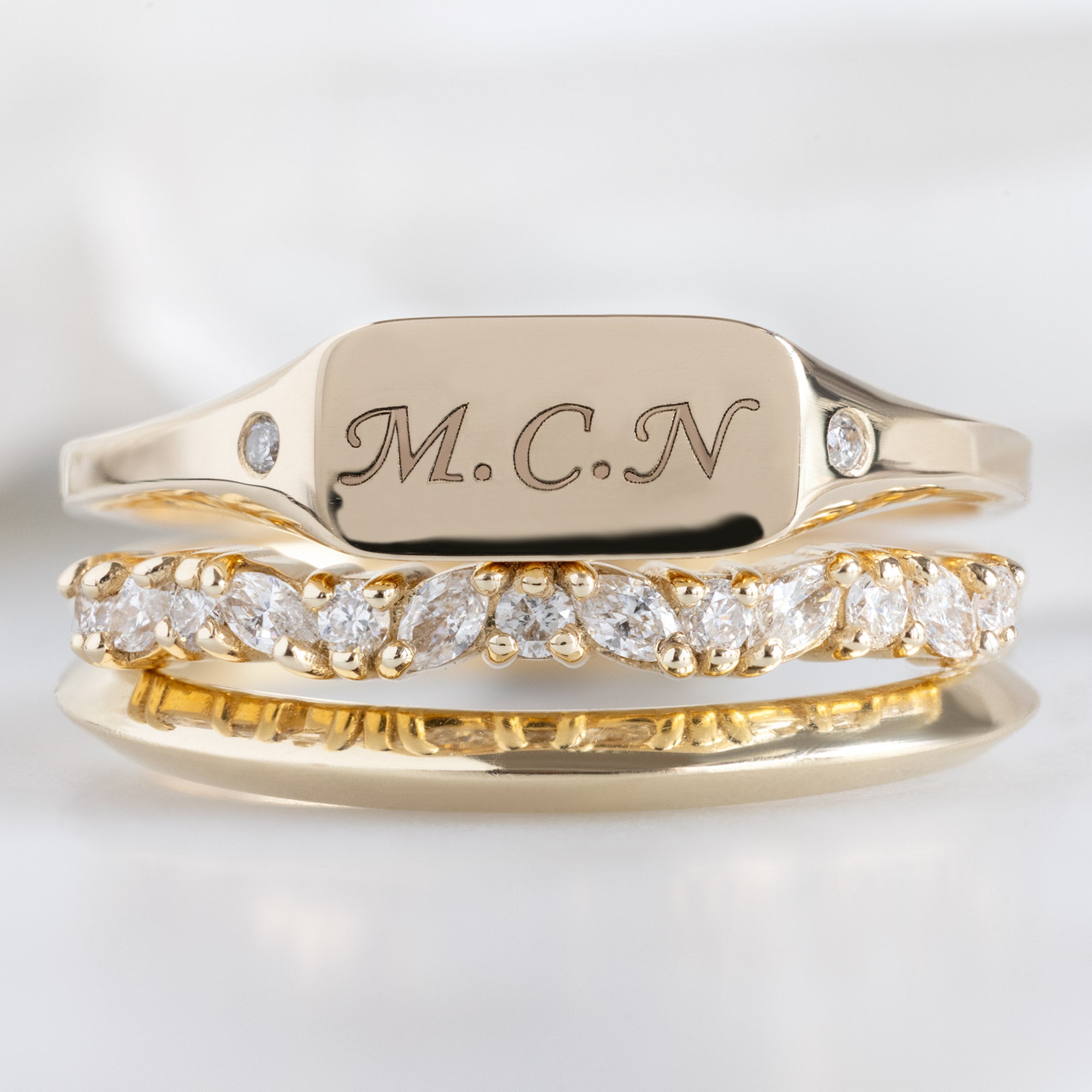 The Monogram Signet Ring in 10K Yellow Gold stacked with yellow gold bands on white marble