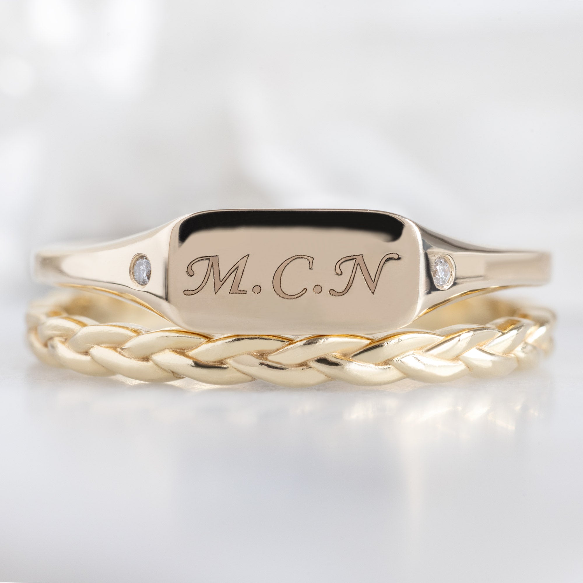 The Monogram Signet Ring in 10K Yellow Gold Stacked with the Braided Stacking Band on White Marble