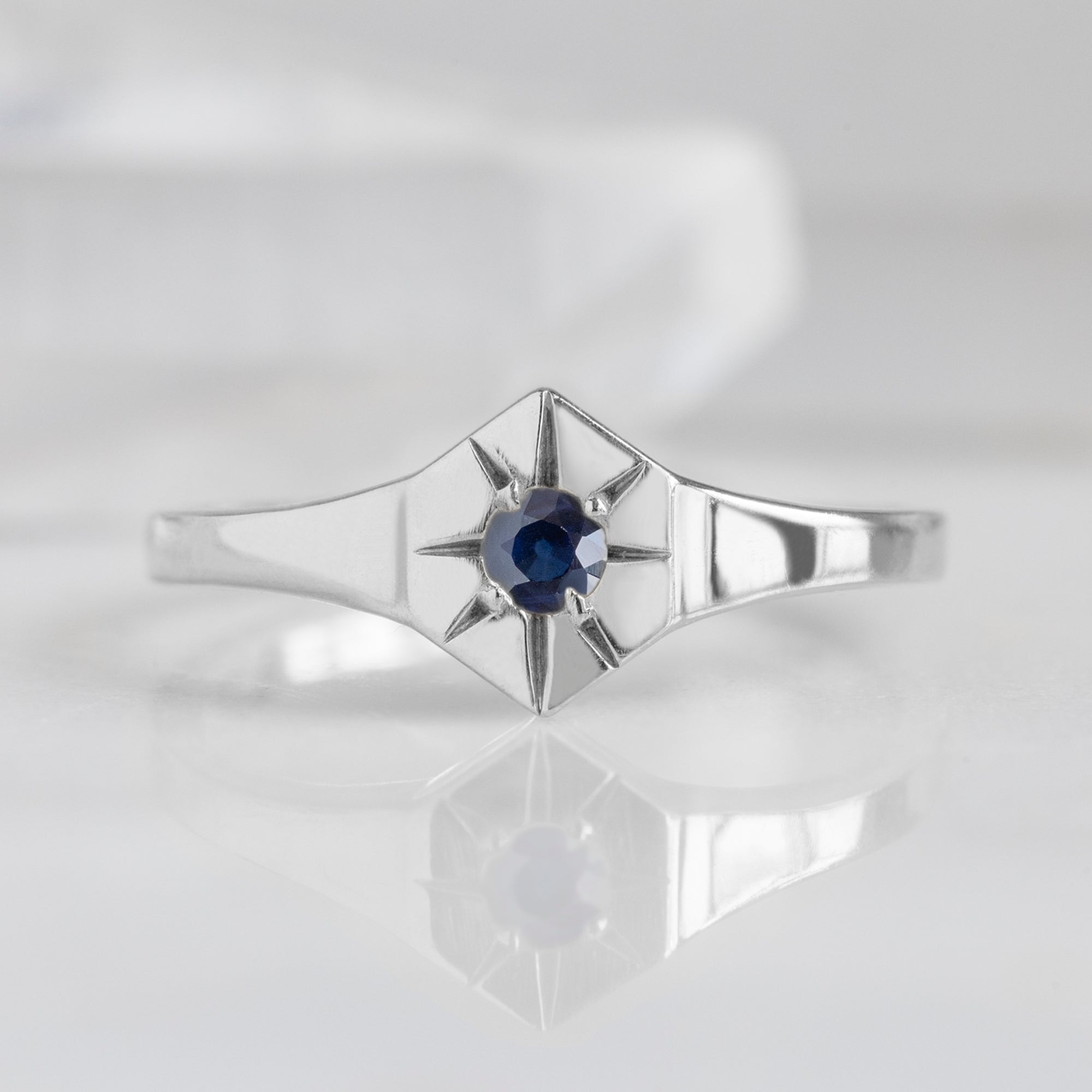 Custom Blue Sapphire Birthstone Signet Ring | 10K White Gold displayed on marble surface with white blurred background.