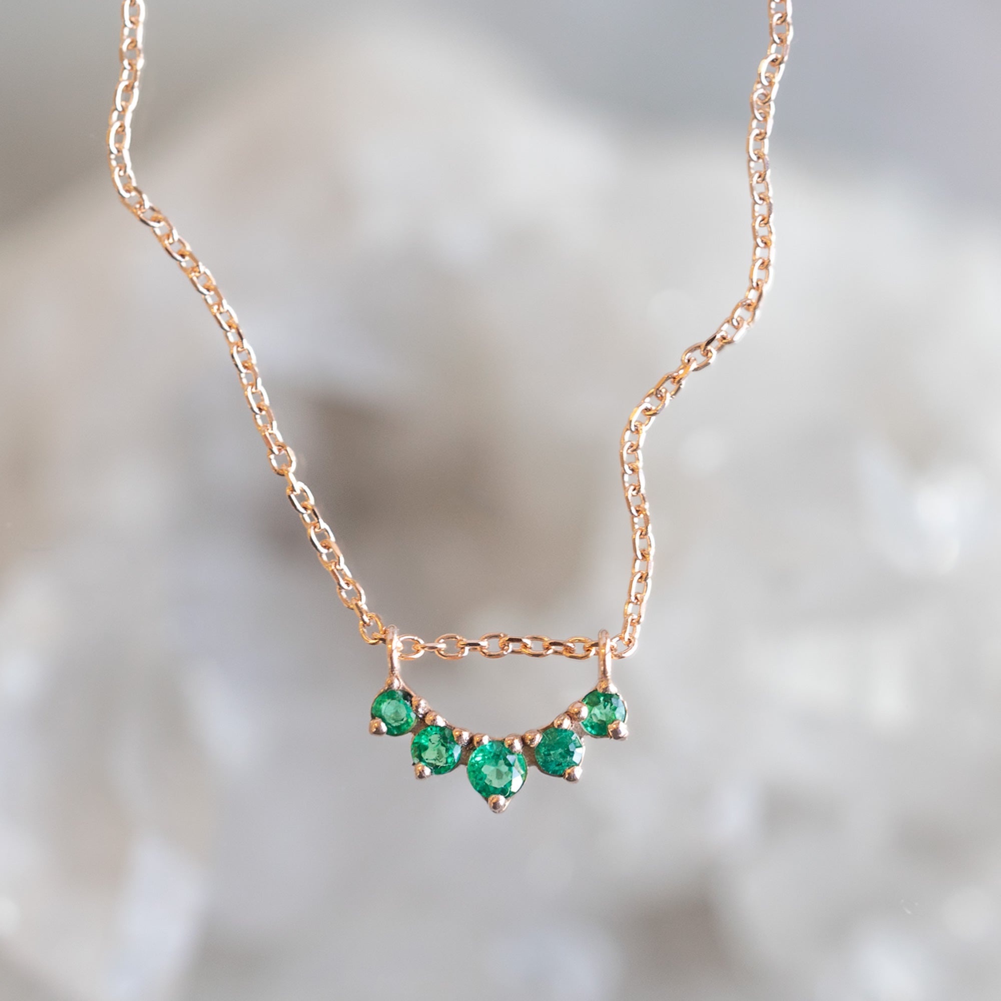 Custom Emerald Gemstone Sunburst Necklace | 10K Rose Gold with blurred background.