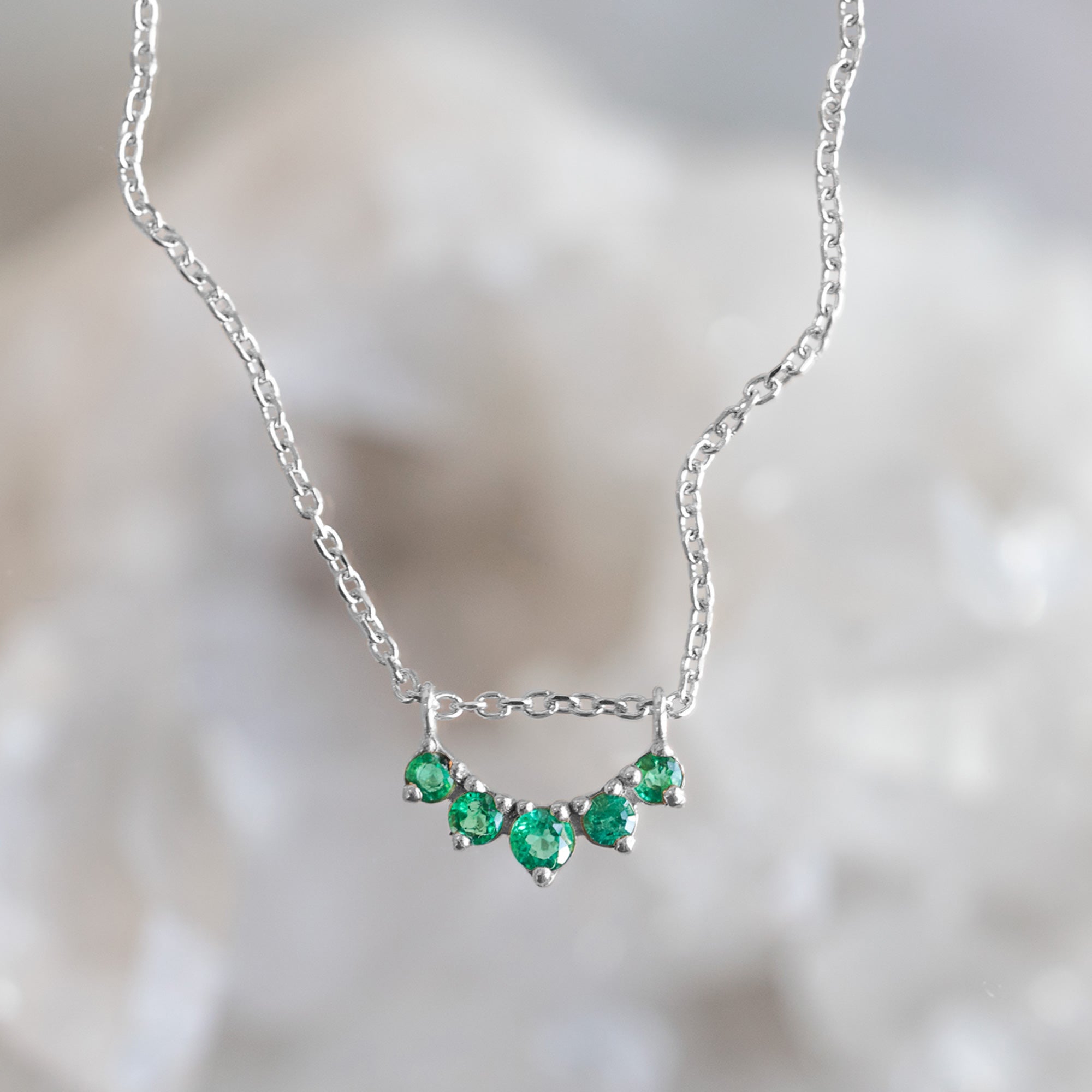Custom Emerald Gemstone Sunburst Necklace in 10K White Gold with blurred background.