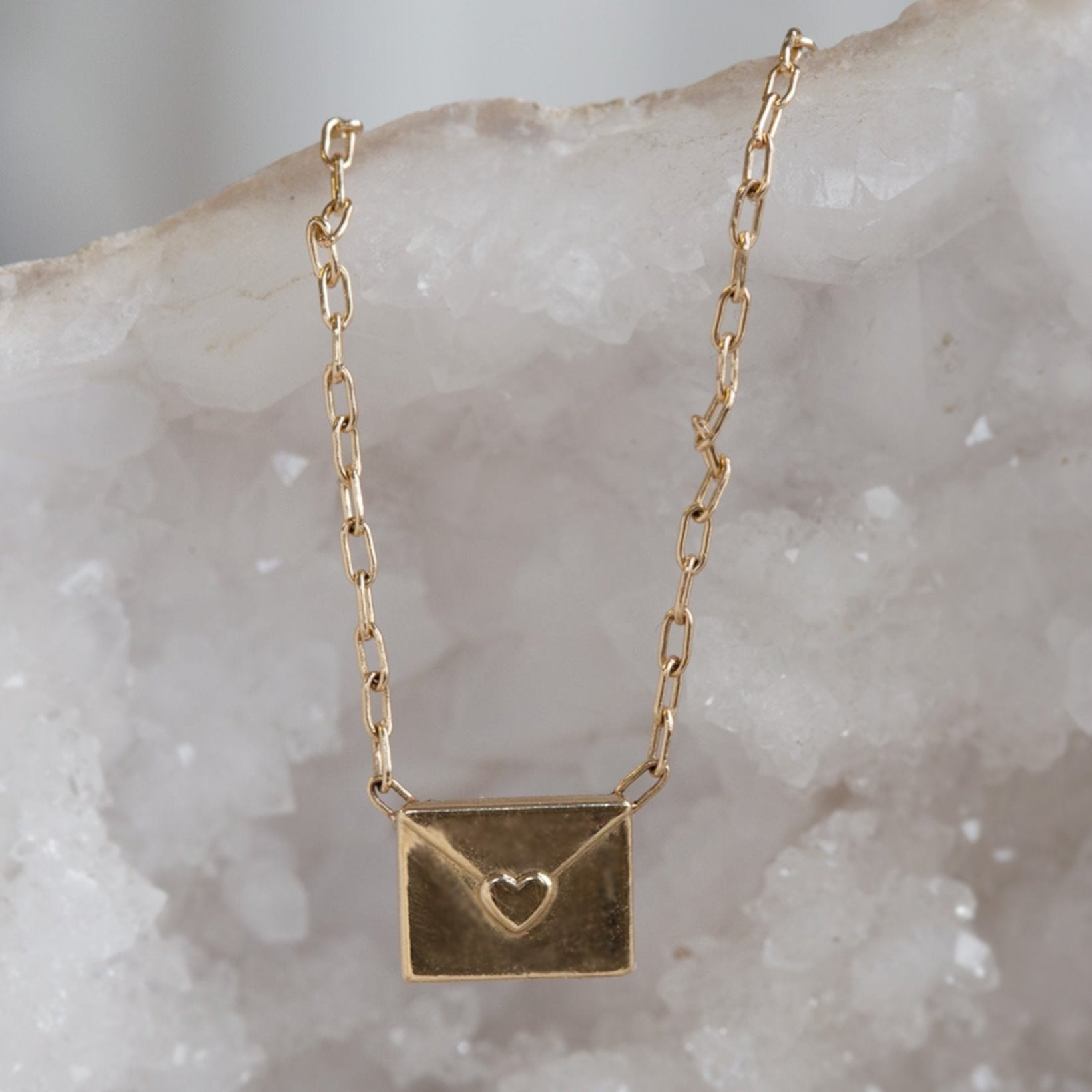 Yellow gold necklace featuring a loveletter shaped pendant hanging on white geode