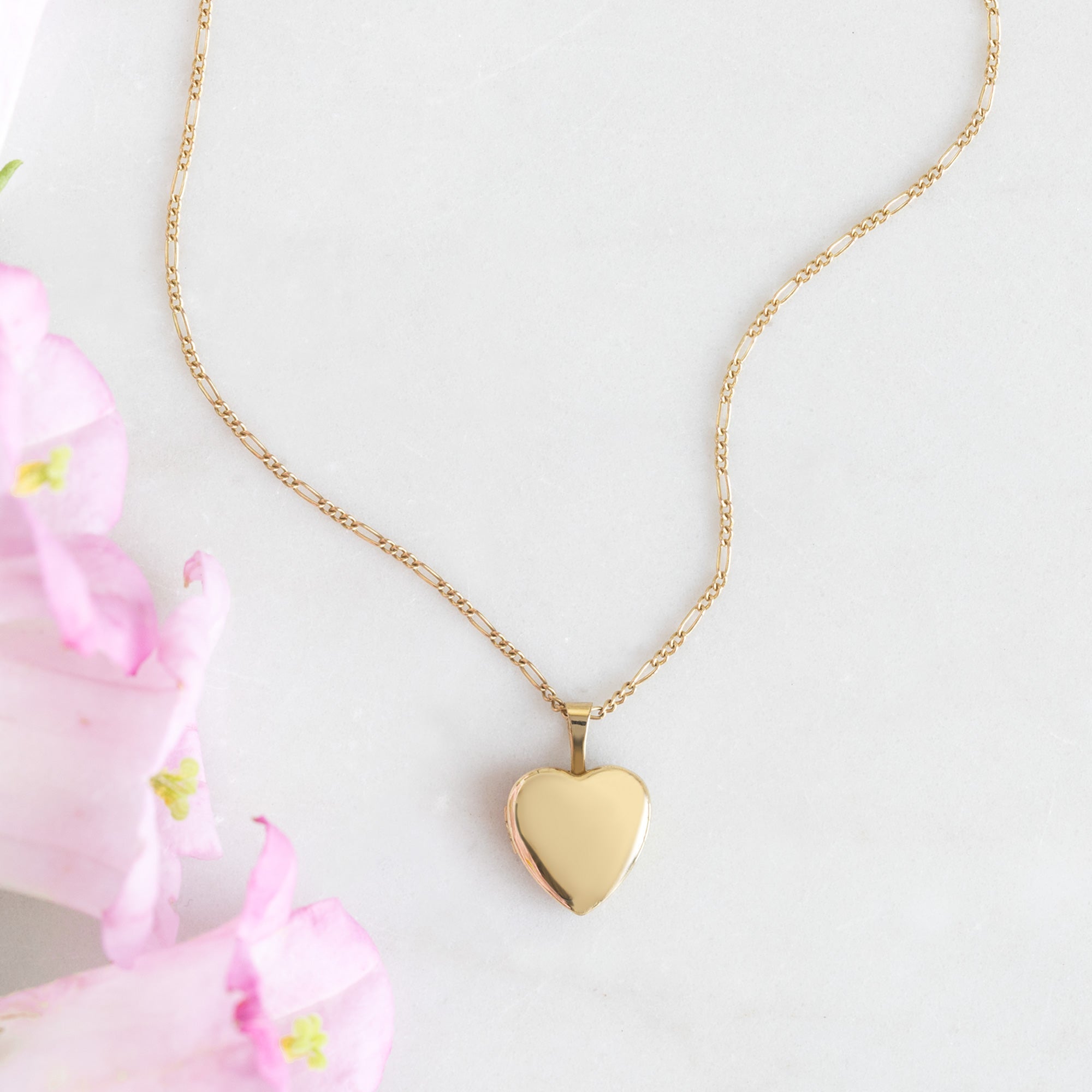 The Yellow Mini Sweetheart Locket Necklace in Yellow Gold on white background with pink flowers