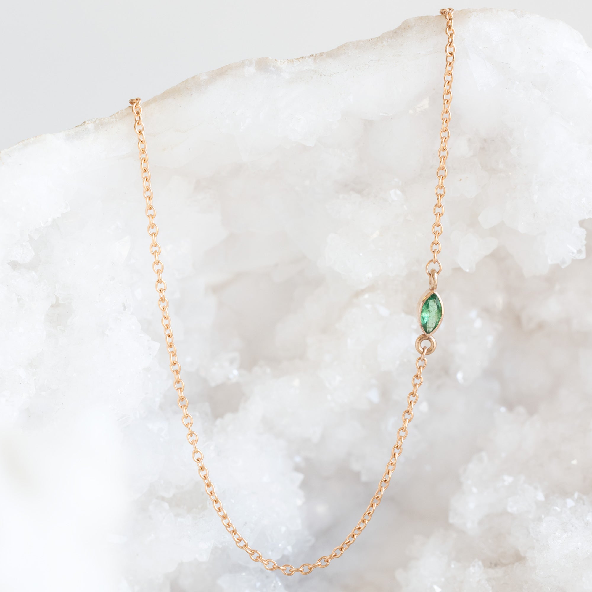 The Teensy Emerald Necklace in Rose Gold Filled hanging on white crystal