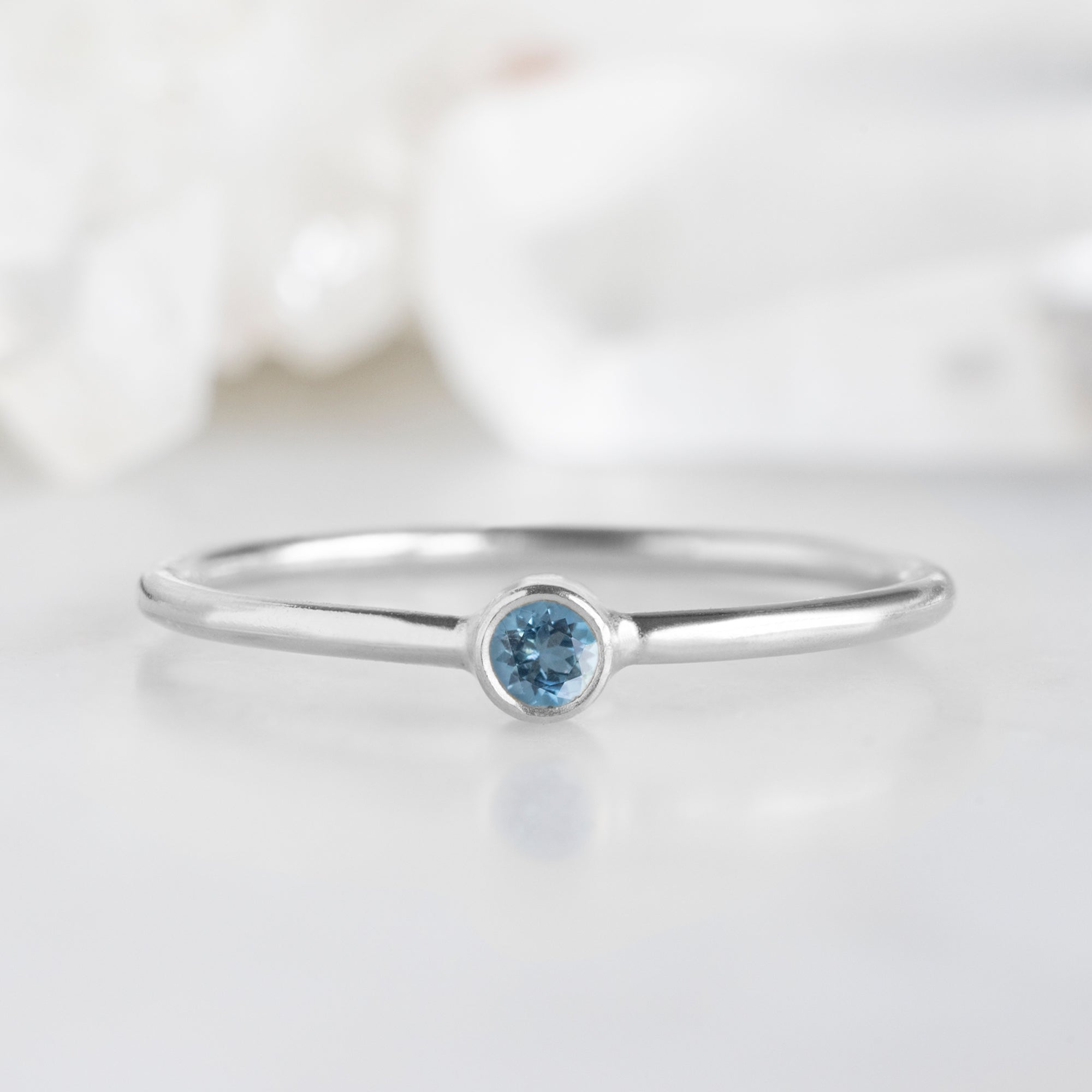Custom Aquamarine Birthstone Stacking Ring | 10K White Gold on marble surface with white blurred background.