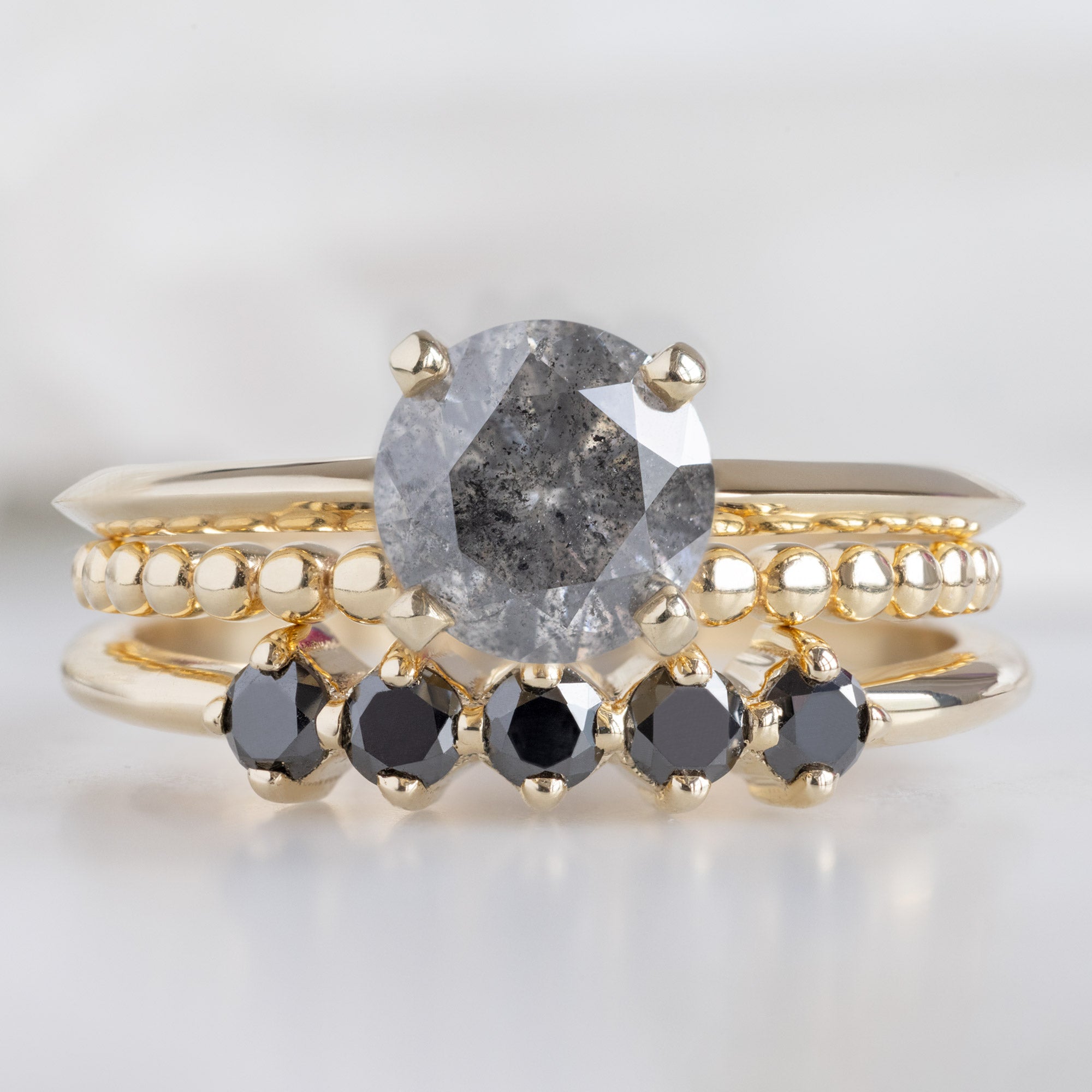 The Sequent Black Diamond Wedding Band in 14K Yellow Gold Stacked with Round Salt and Pepper Diamond Engagement Ring on White Marble