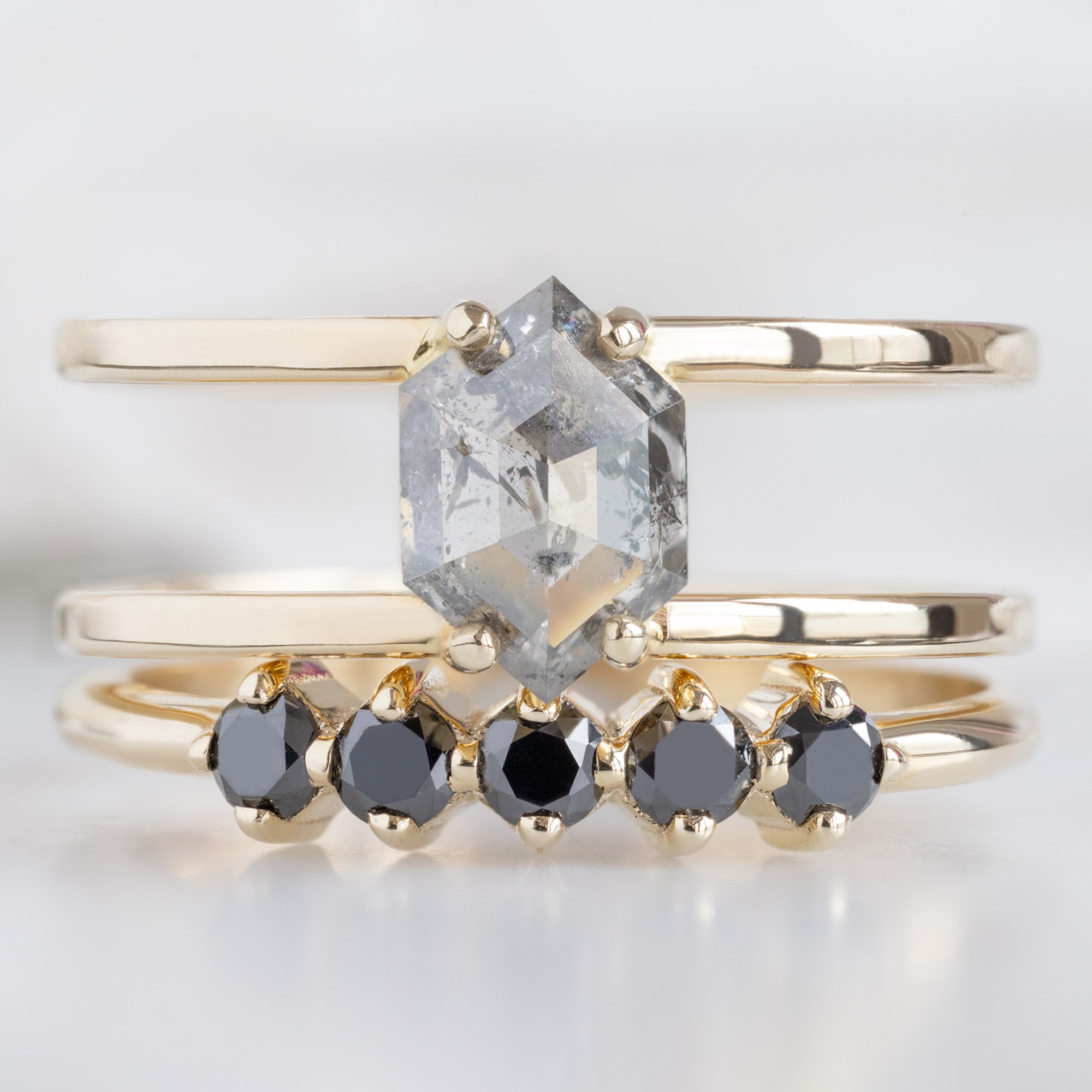 The Sequent Black Diamond Wedding Band in 14K Yellow Gold Stacked with Double Band Salt and Pepper Diamond Engagement Ring on White Marble
