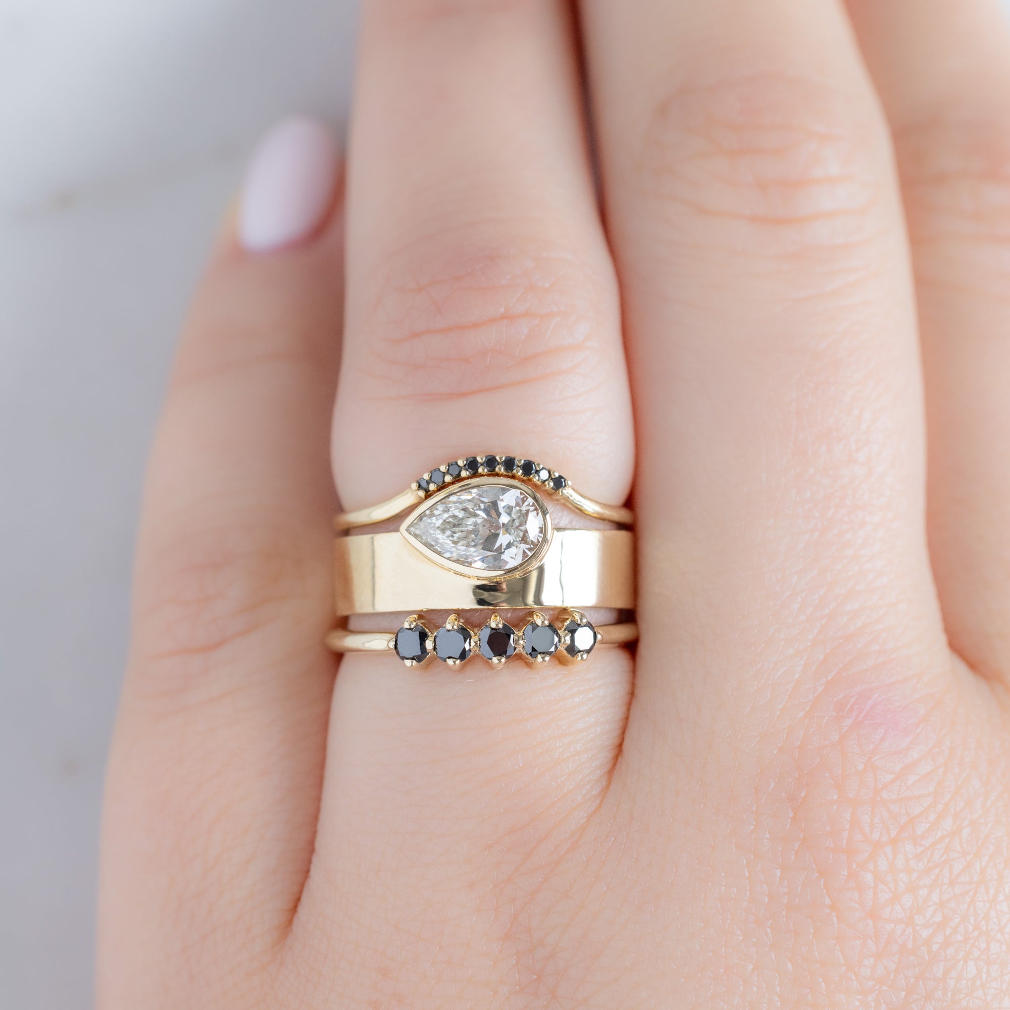 The Sequent Black Diamond Wedding Band in 14K Yellow Gold Stacked with White Diamond Cigar Engagement Ring on Model