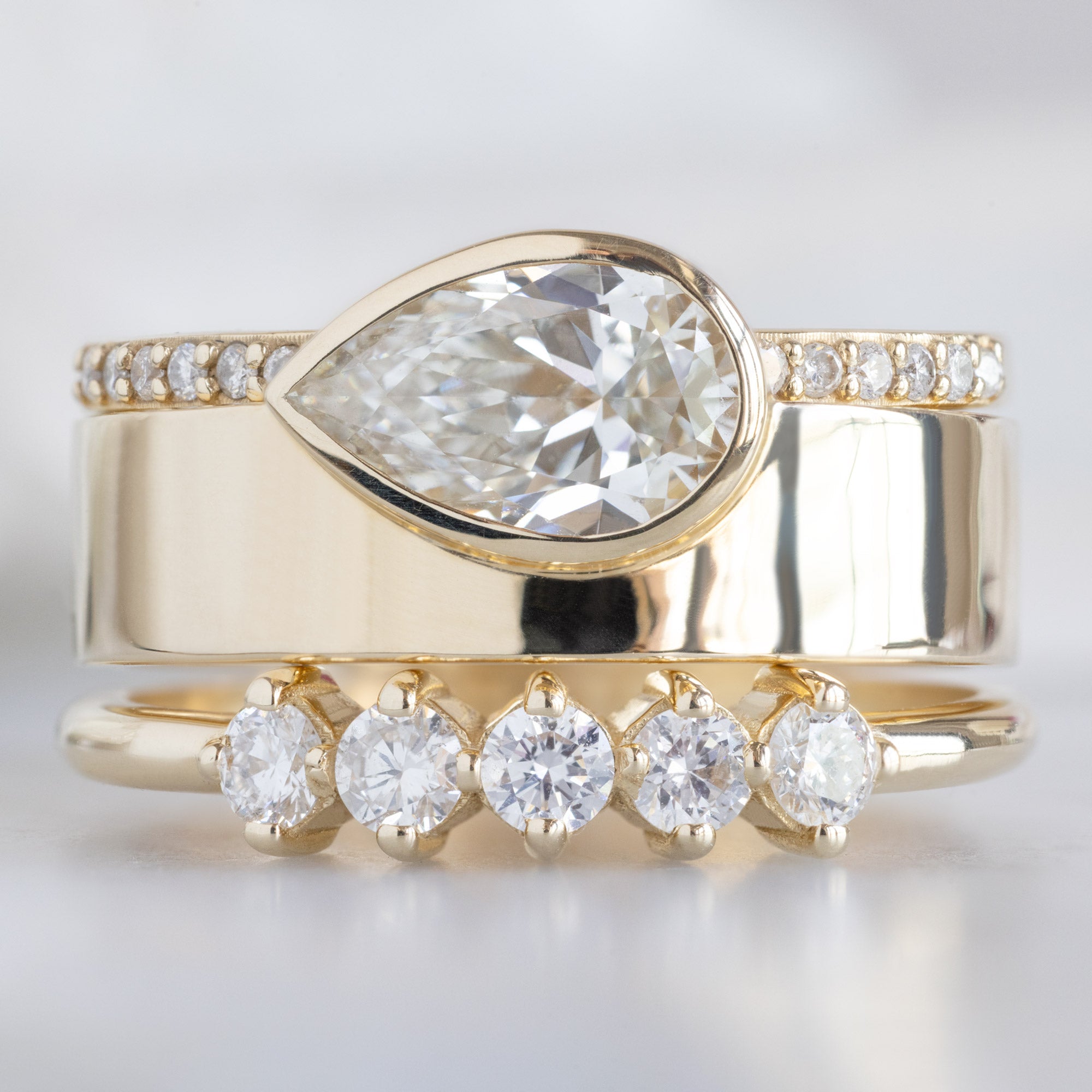 The Sequent White Diamond Wedding Band in 14K Yellow Gold Stacked with White Diamond Cigar Engagement Ring on White Marble
